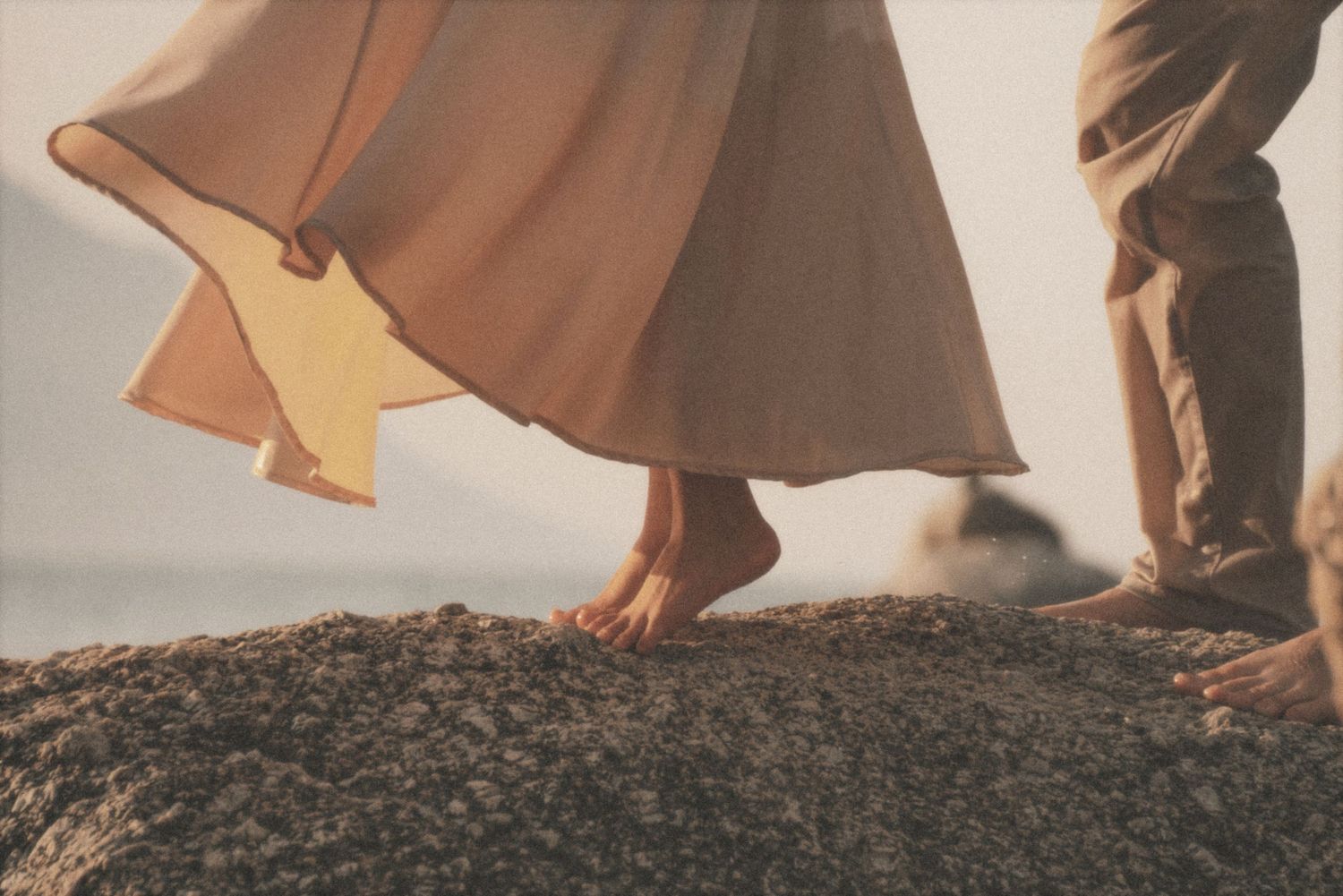 Detail of a barefoot woman's flowing cream skirt swirling as she stands on a rock