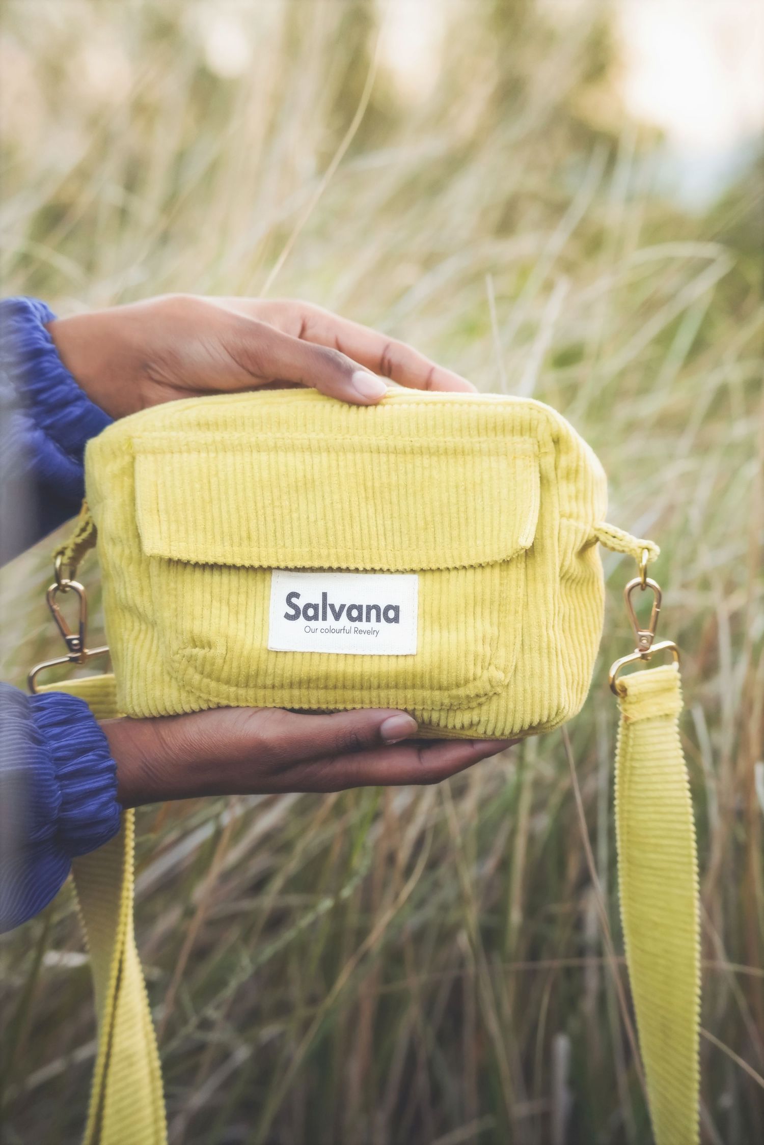 Hands holding a yellow Salvana corduroy bag in front of tall golden grass