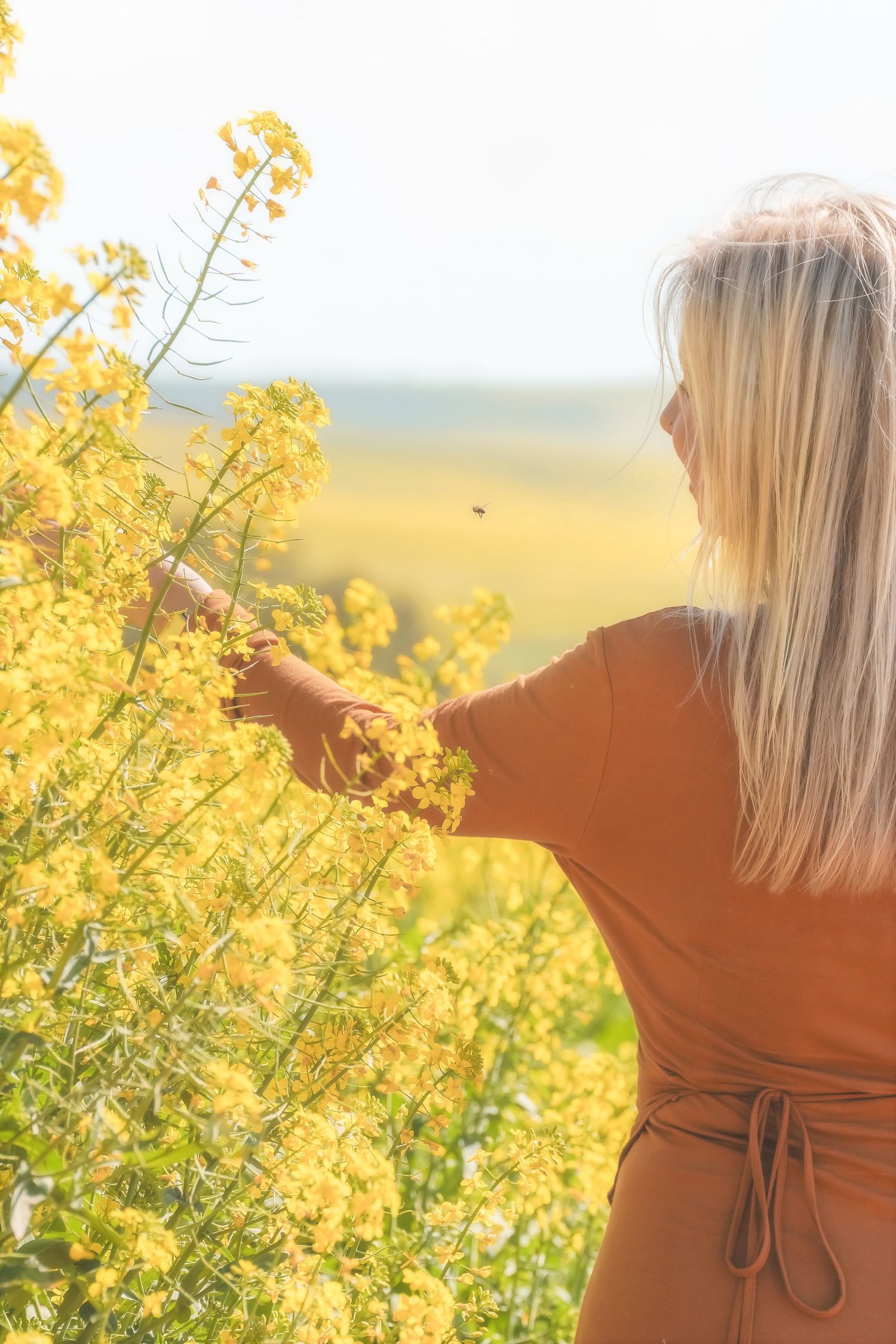Woman in a rust dress reaching out to touch canola flowers