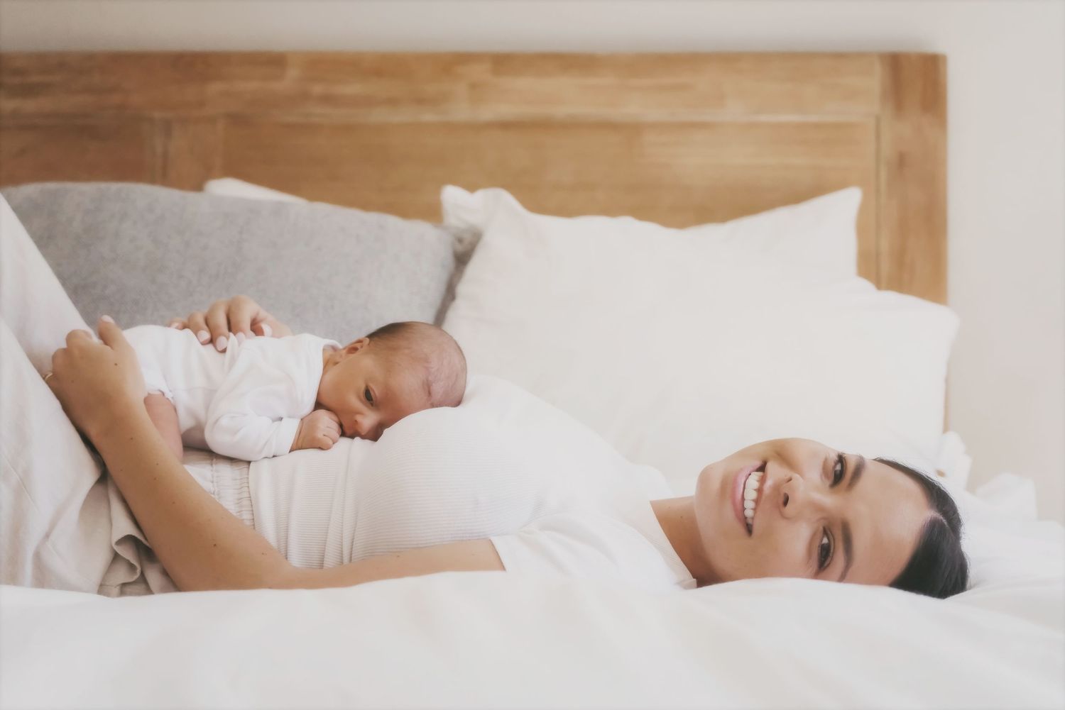 Smiling mother lying on a bed with her newborn resting on her chest
