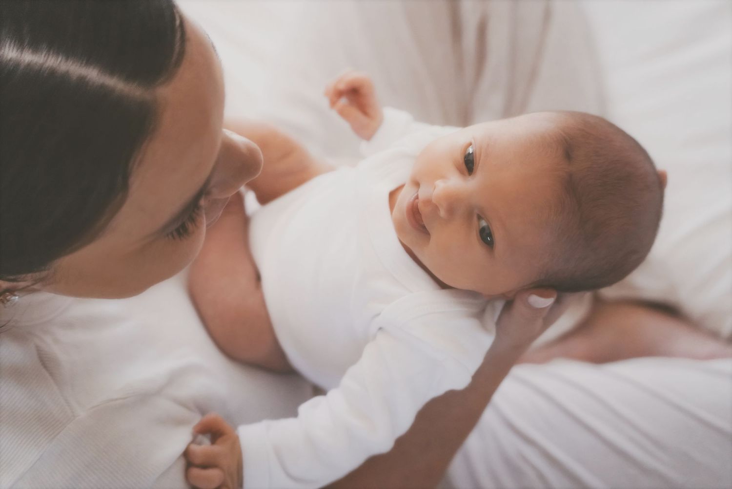 Mother leaning over her newborn on a white bed as they gaze up at her