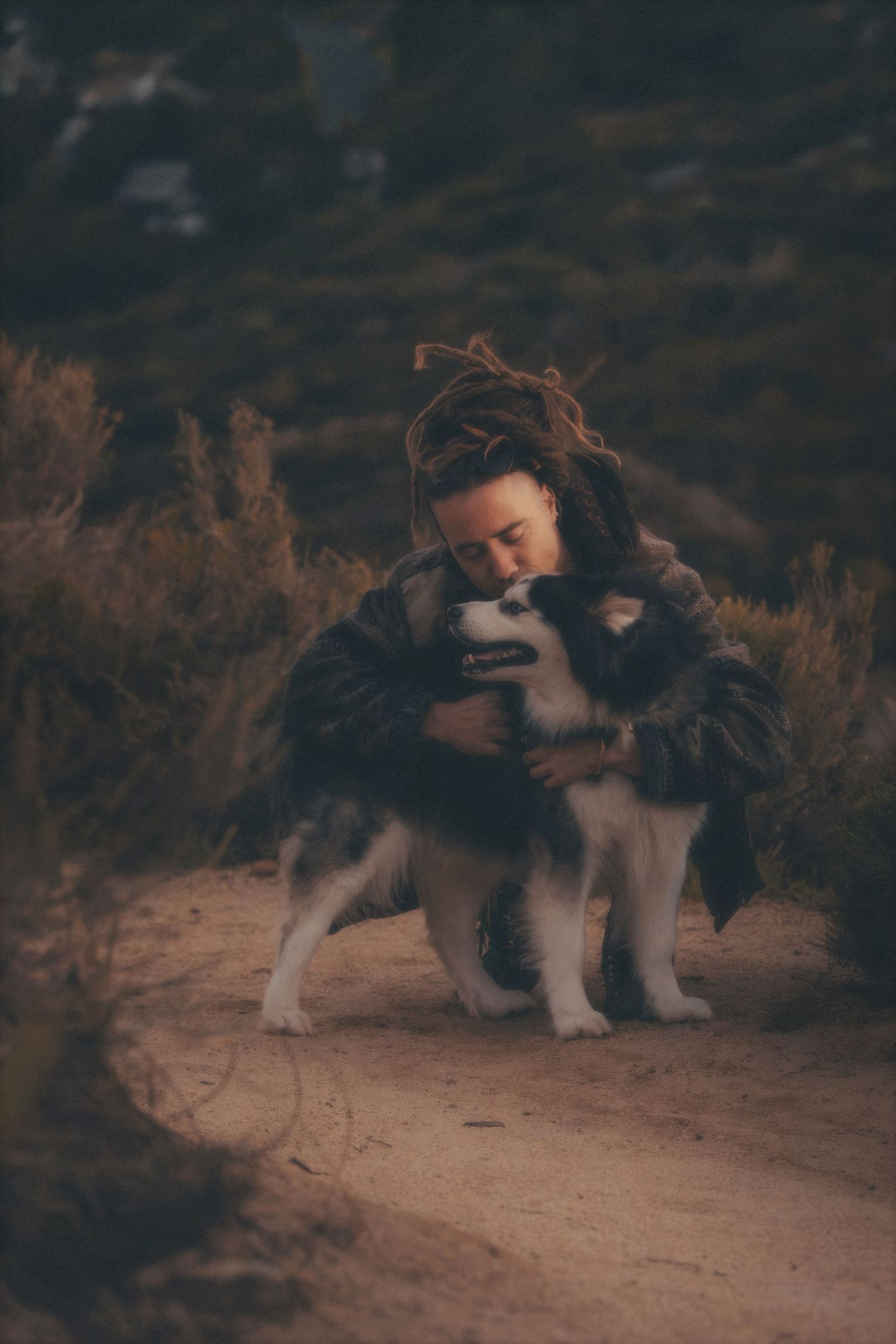 Man hugging his husky on a sandy fynbos trail in the mountains