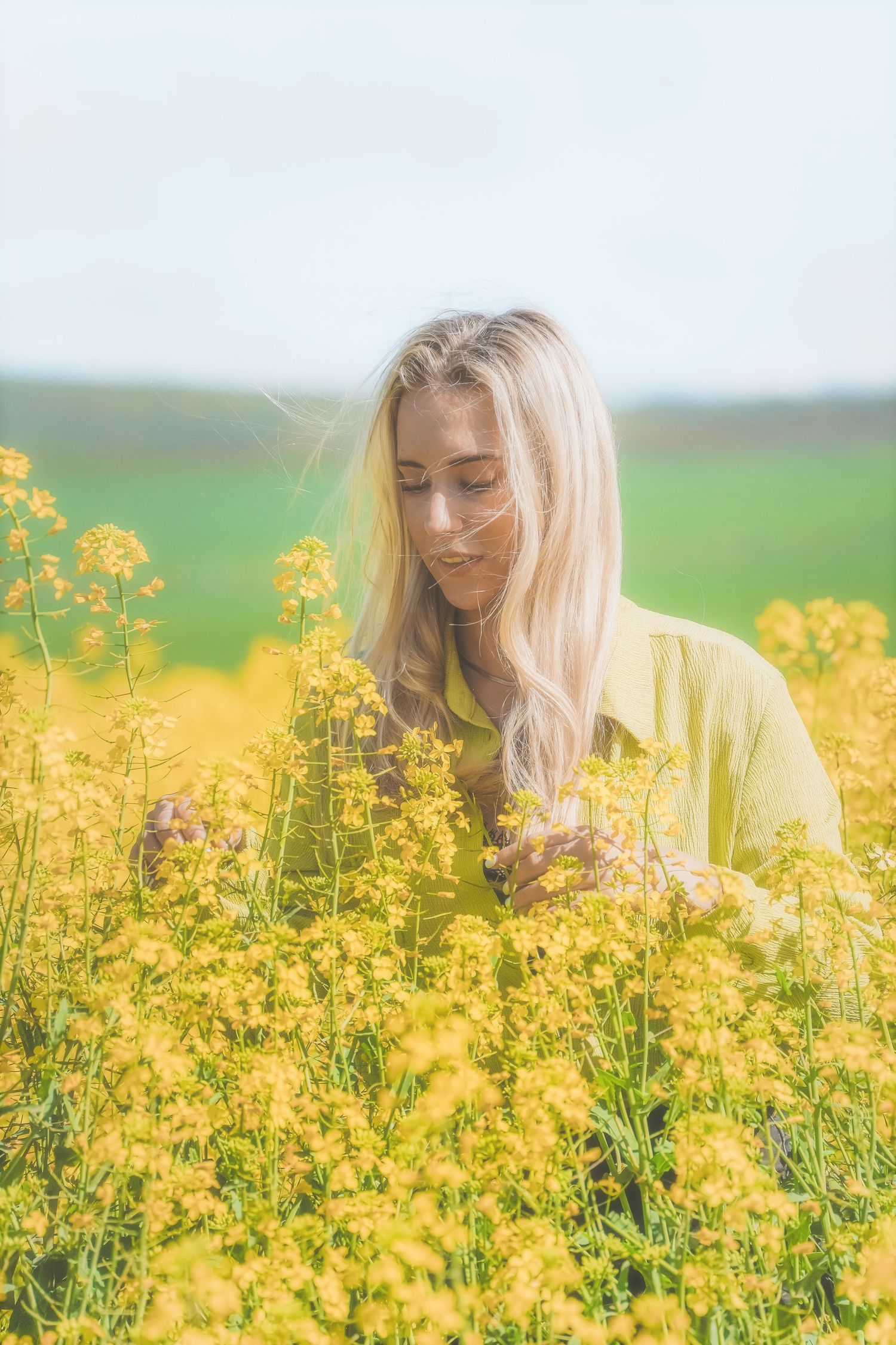 Woman in a lime green shirt touching canola flowers, green hills behind