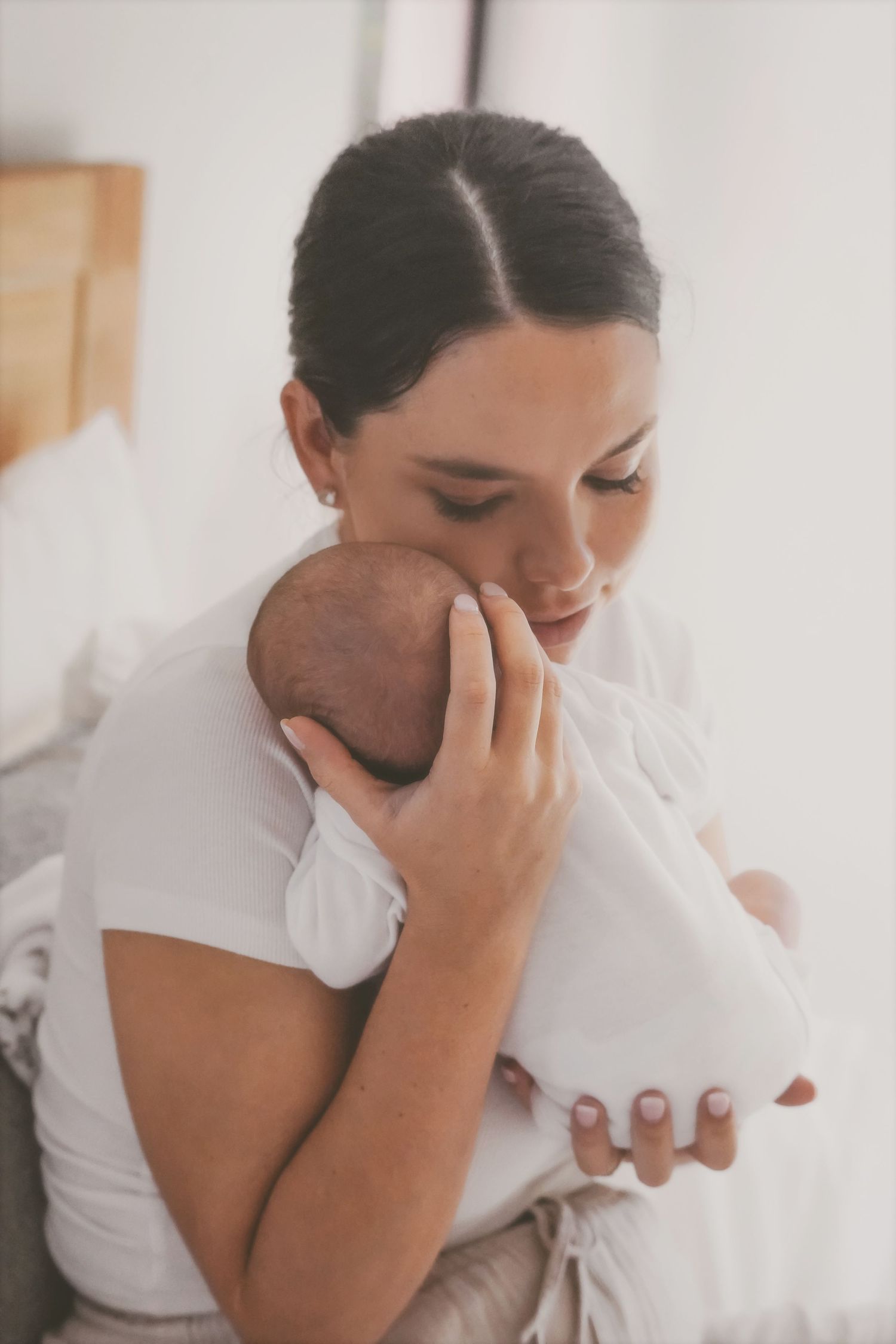 Mother holding her newborn against her cheek in a quiet, tender moment