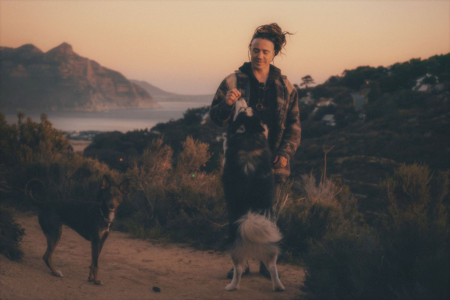 Man walking his husky along a mountain trail with the sea and mountains behind