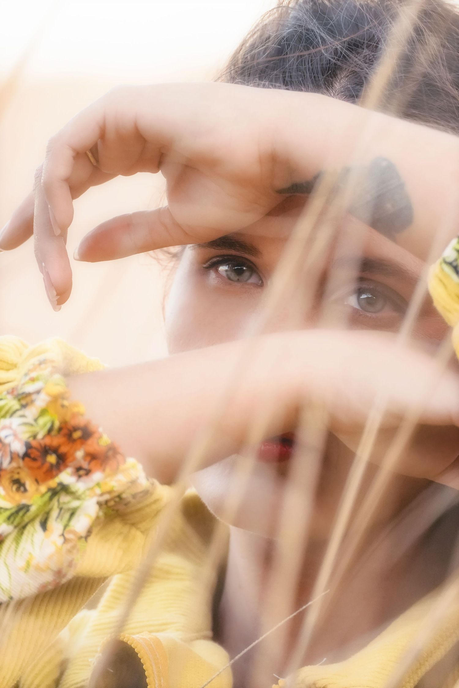 Close-up of a woman's eye framed by her hands through blades of grass