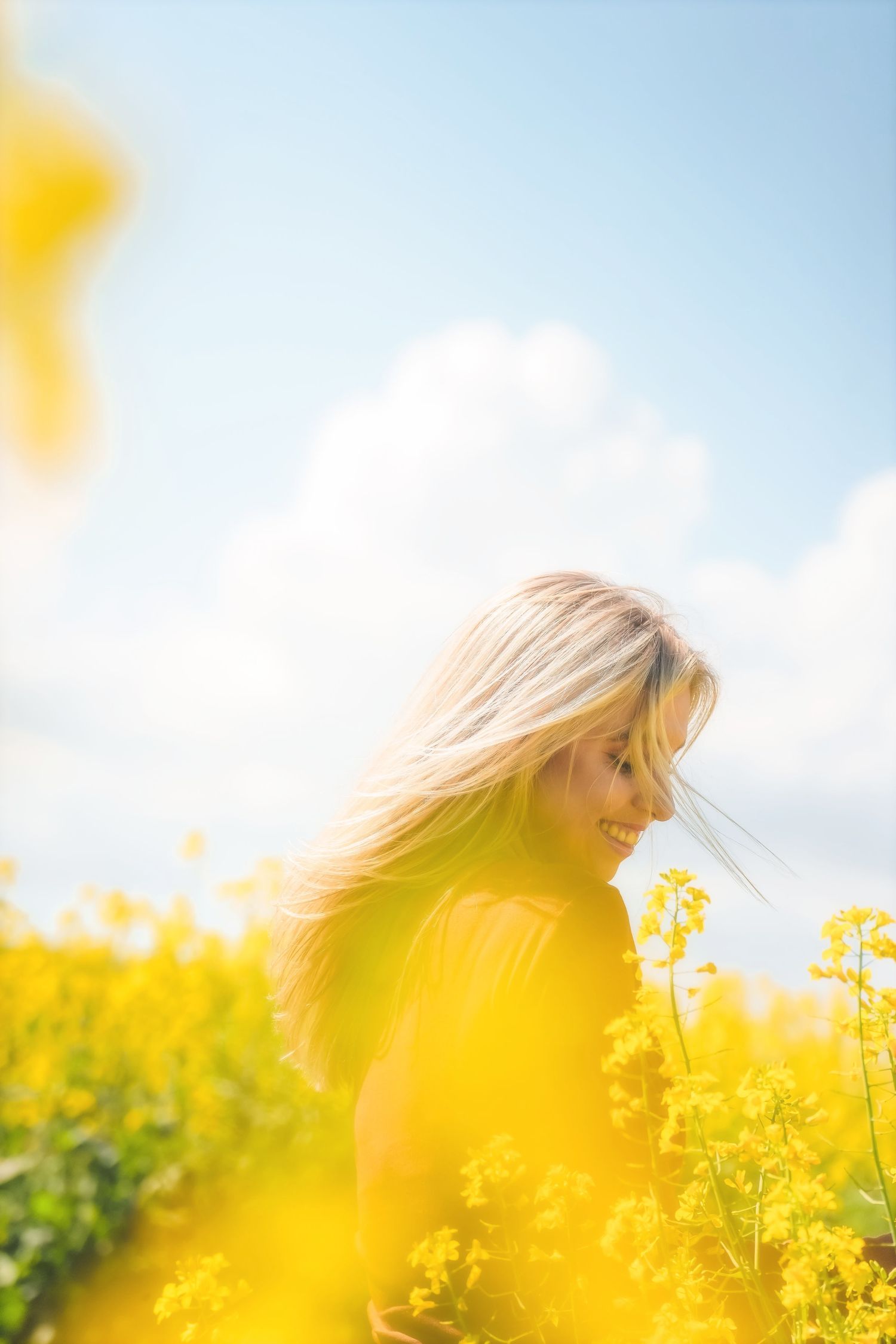 Smiling woman with wind-blown hair among blurred yellow canola, under a blue sky