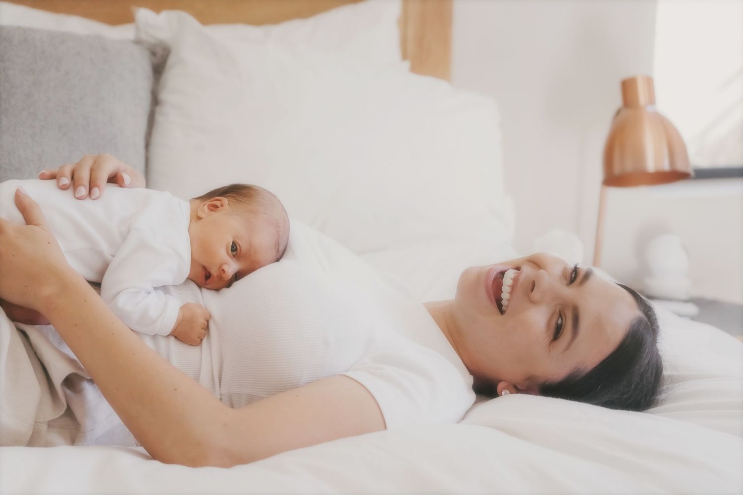 Laughing mother lying on a bed with her newborn on her chest