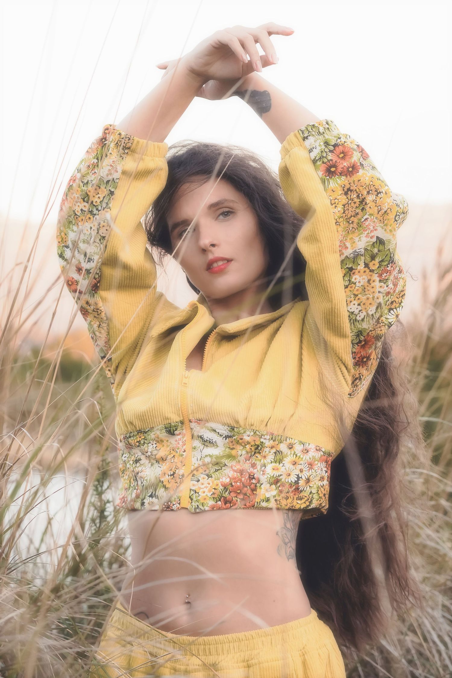 Woman in a yellow floral cropped jacket raising her arms above her head in tall grass, Somerset West
