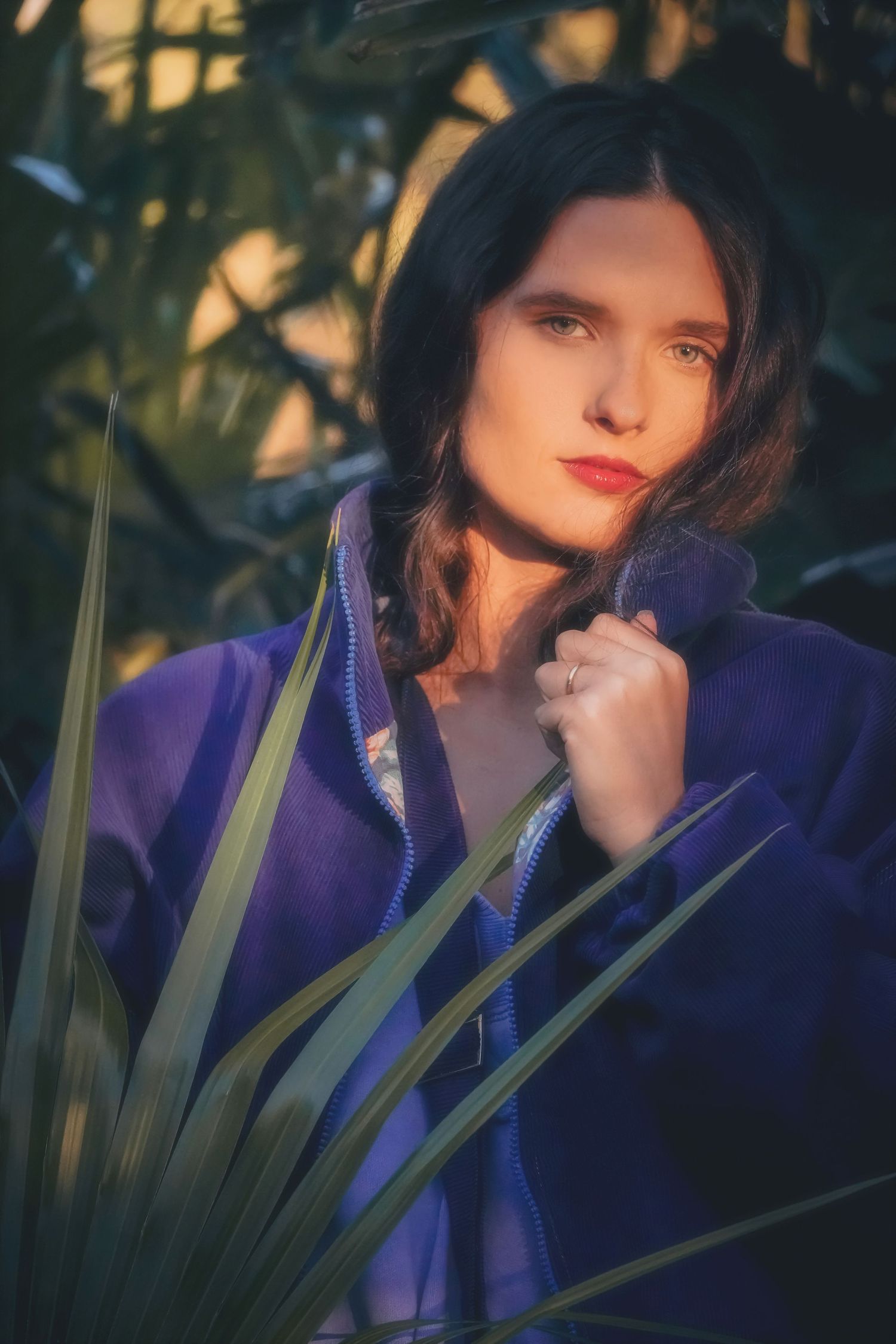 Portrait of a woman in a purple jacket holding her collar among palm leaves