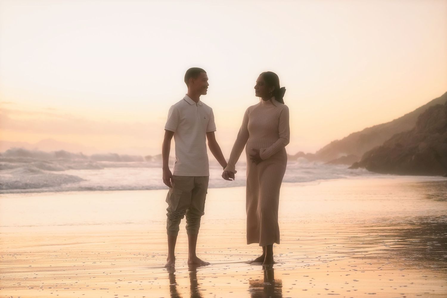 Couple standing hand in hand on the sand at sunset
