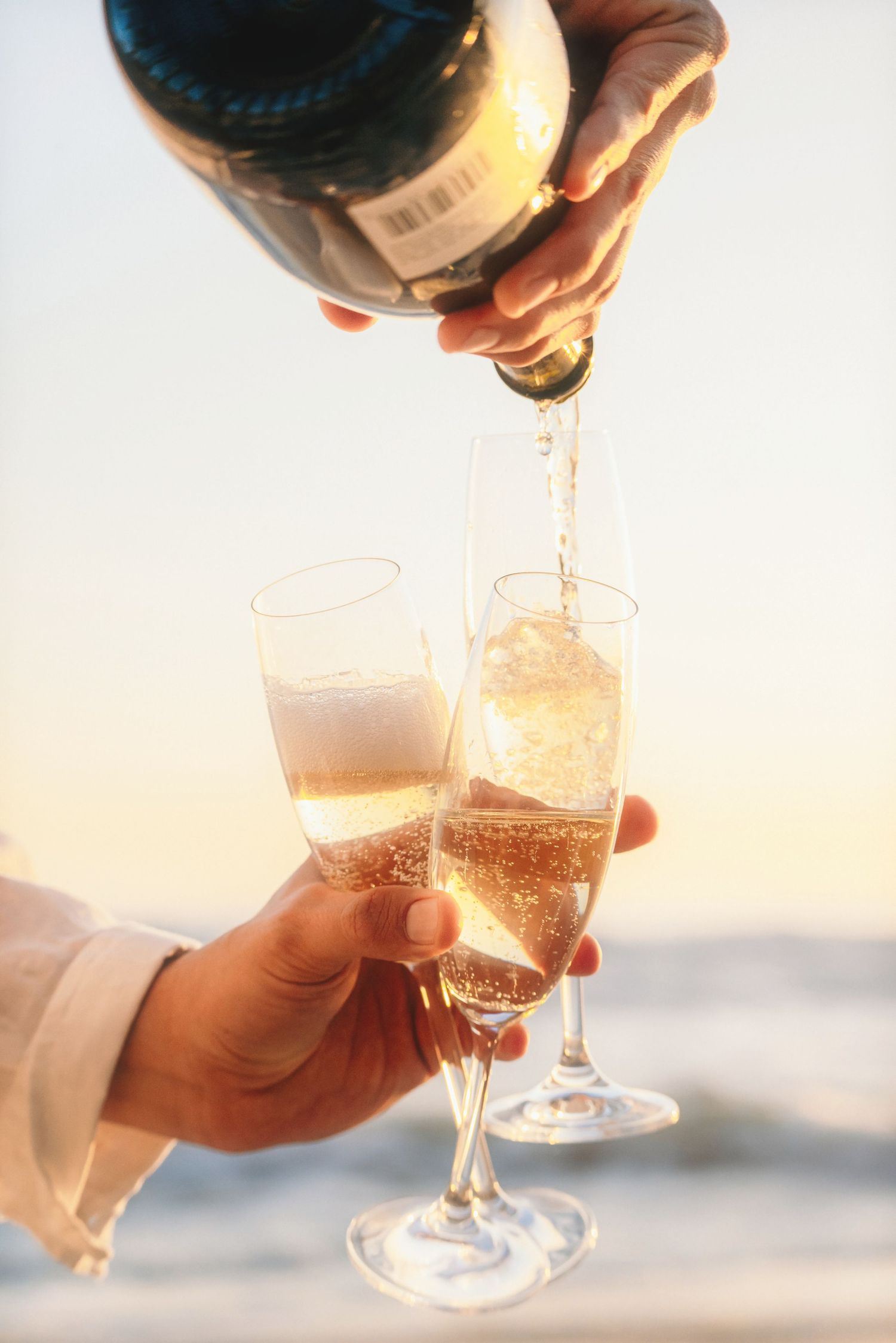 Hands pouring champagne into two glasses with the ocean softly blurred behind