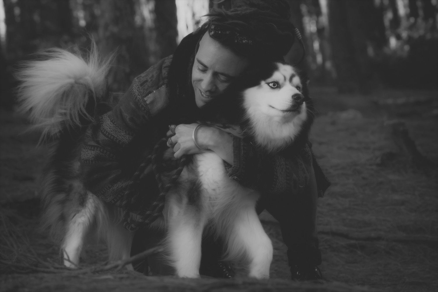 Black and white photo of a man hugging his husky in the forest