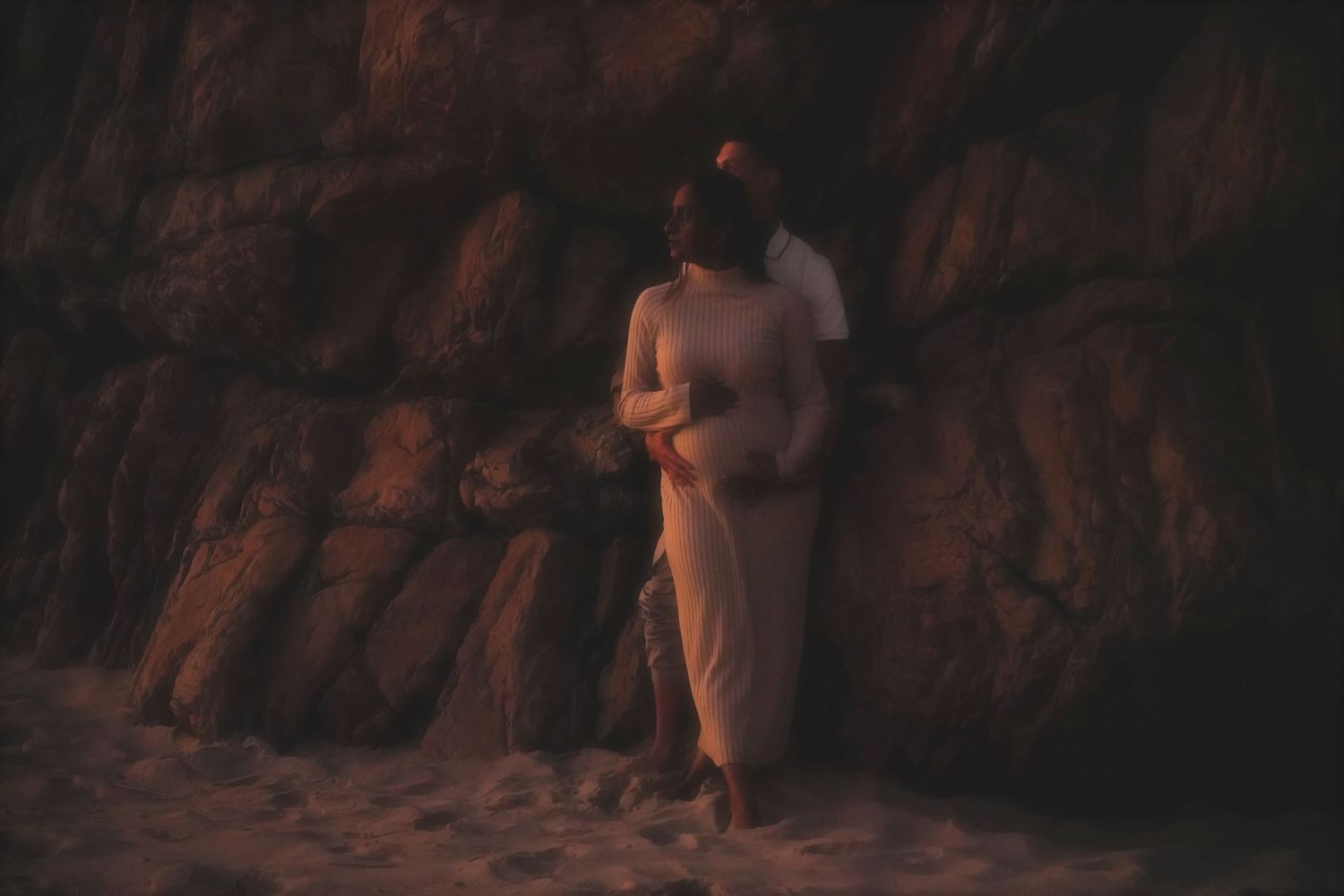 Pregnant woman leaning against a rock face with her partner behind her