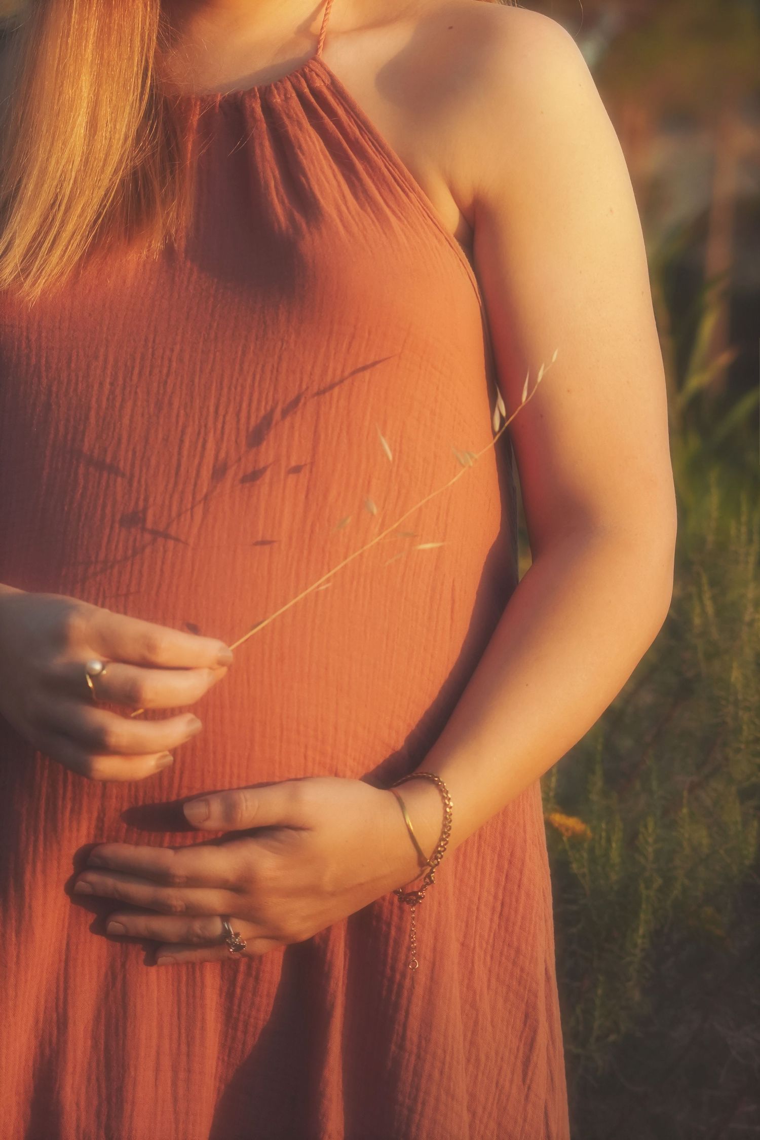 Close-up of a pregnant belly in a terracotta dress, hands resting on the bump