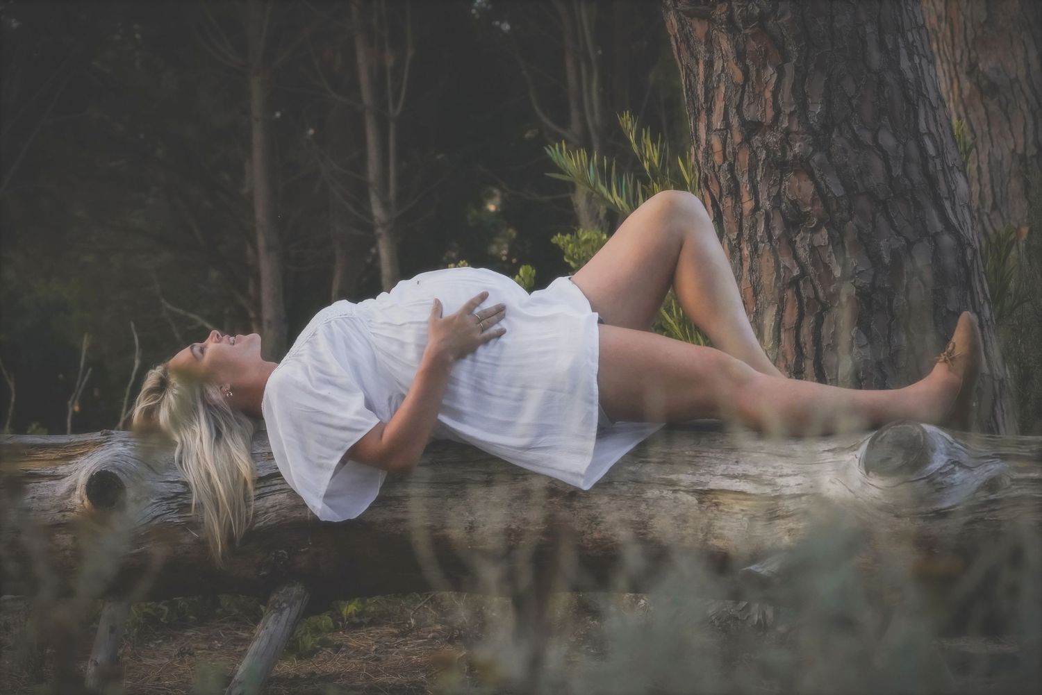 Pregnant woman lying on a fallen log with her hand on her bump