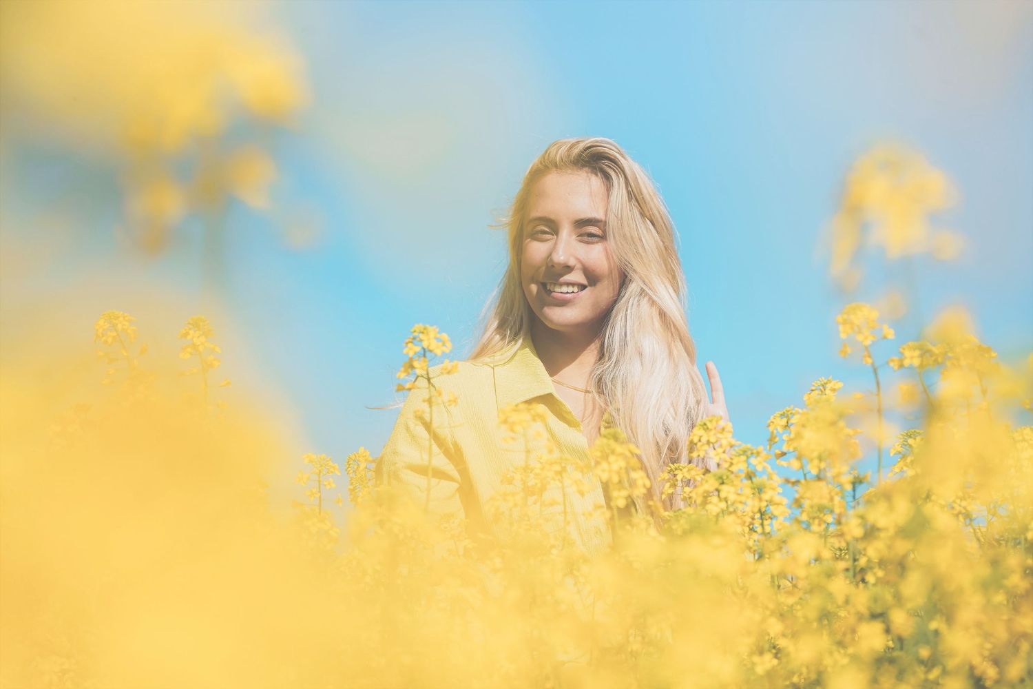 Smiling woman standing in a canola field beneath a blue sky