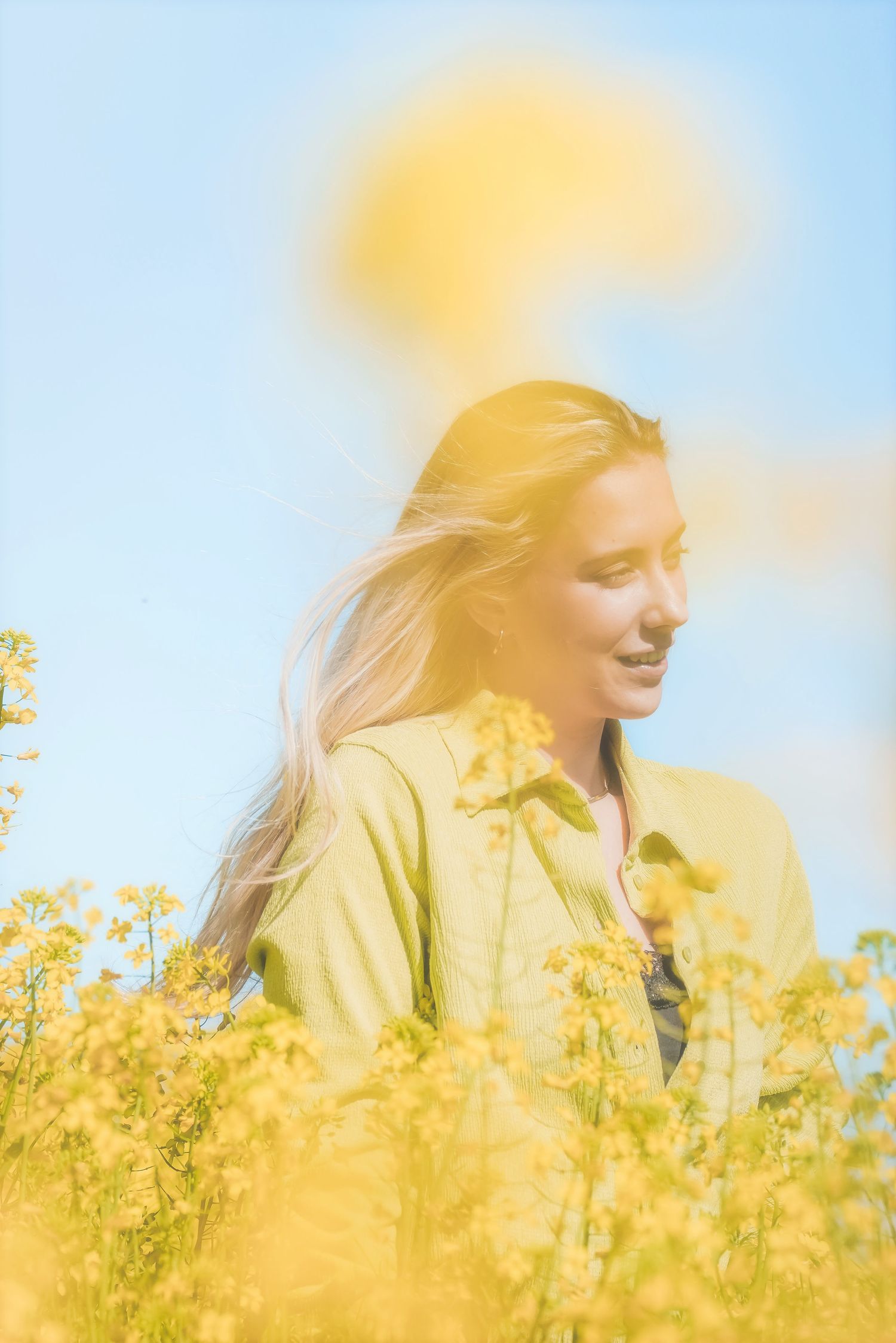 Woman in a lime green shirt with wind-blown hair, smiling to the side against a blue sky