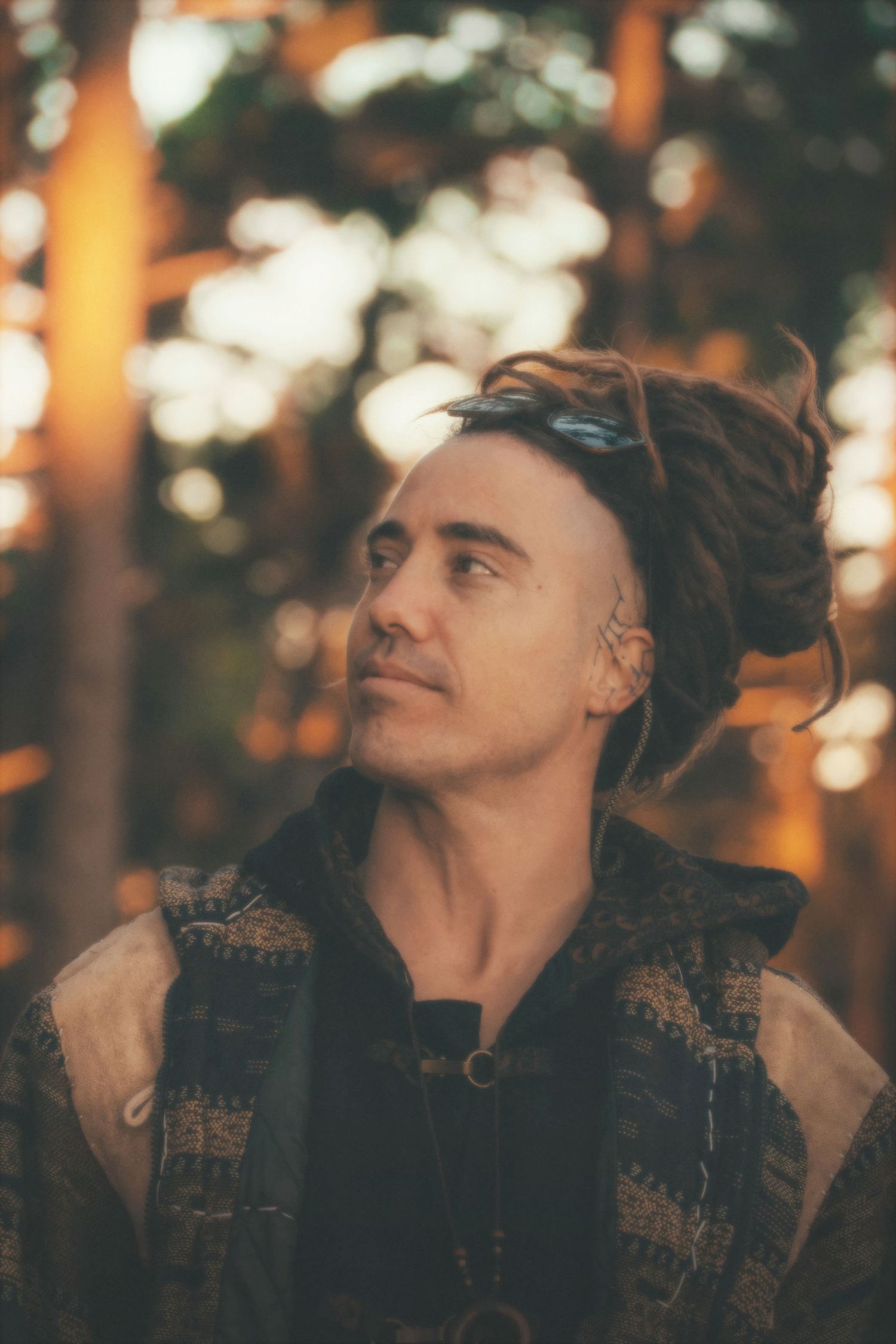 Portrait of a man with dreadlocks gazing up through golden forest light