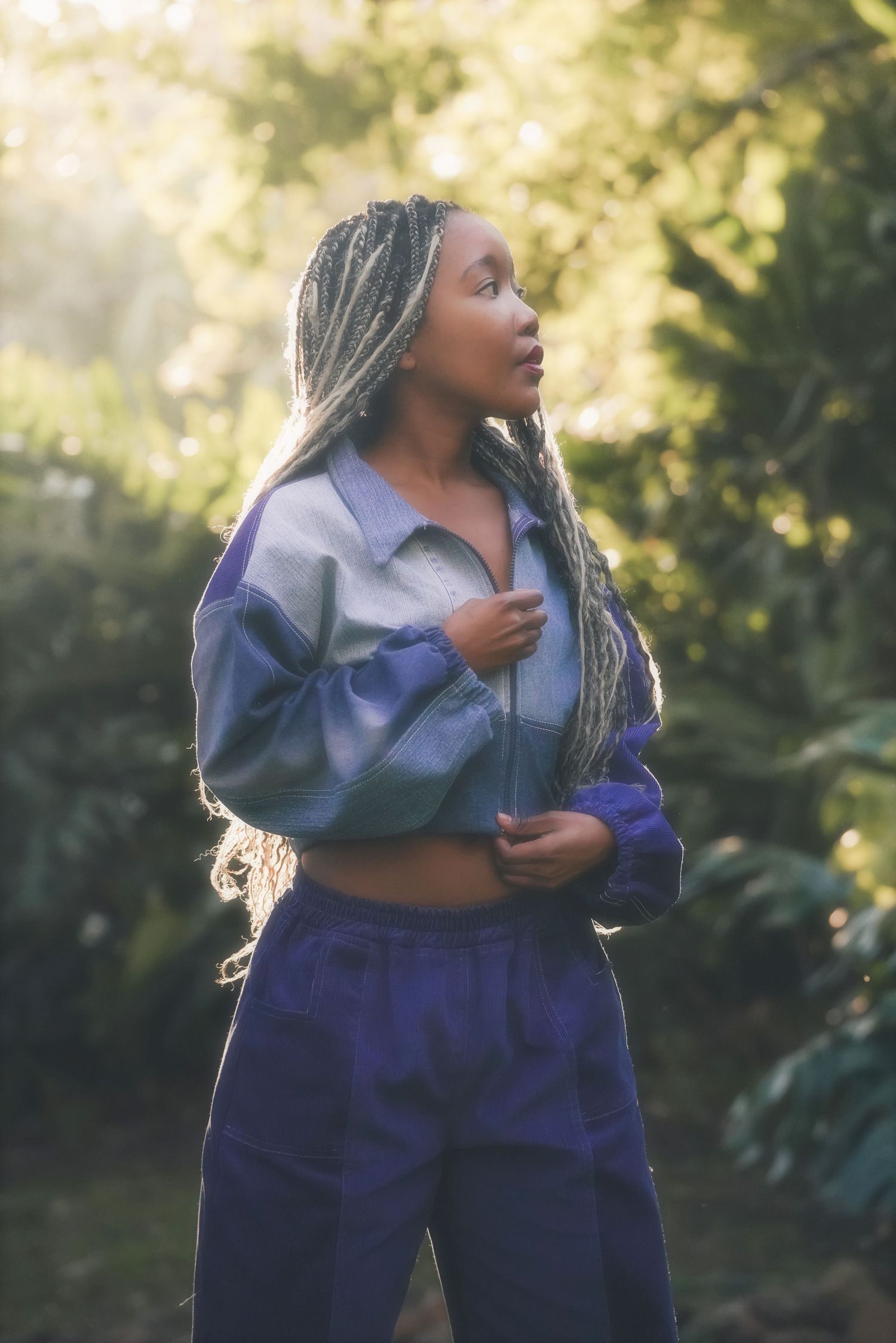 Woman with long braids in a blue jacket looking aside in soft, leafy light