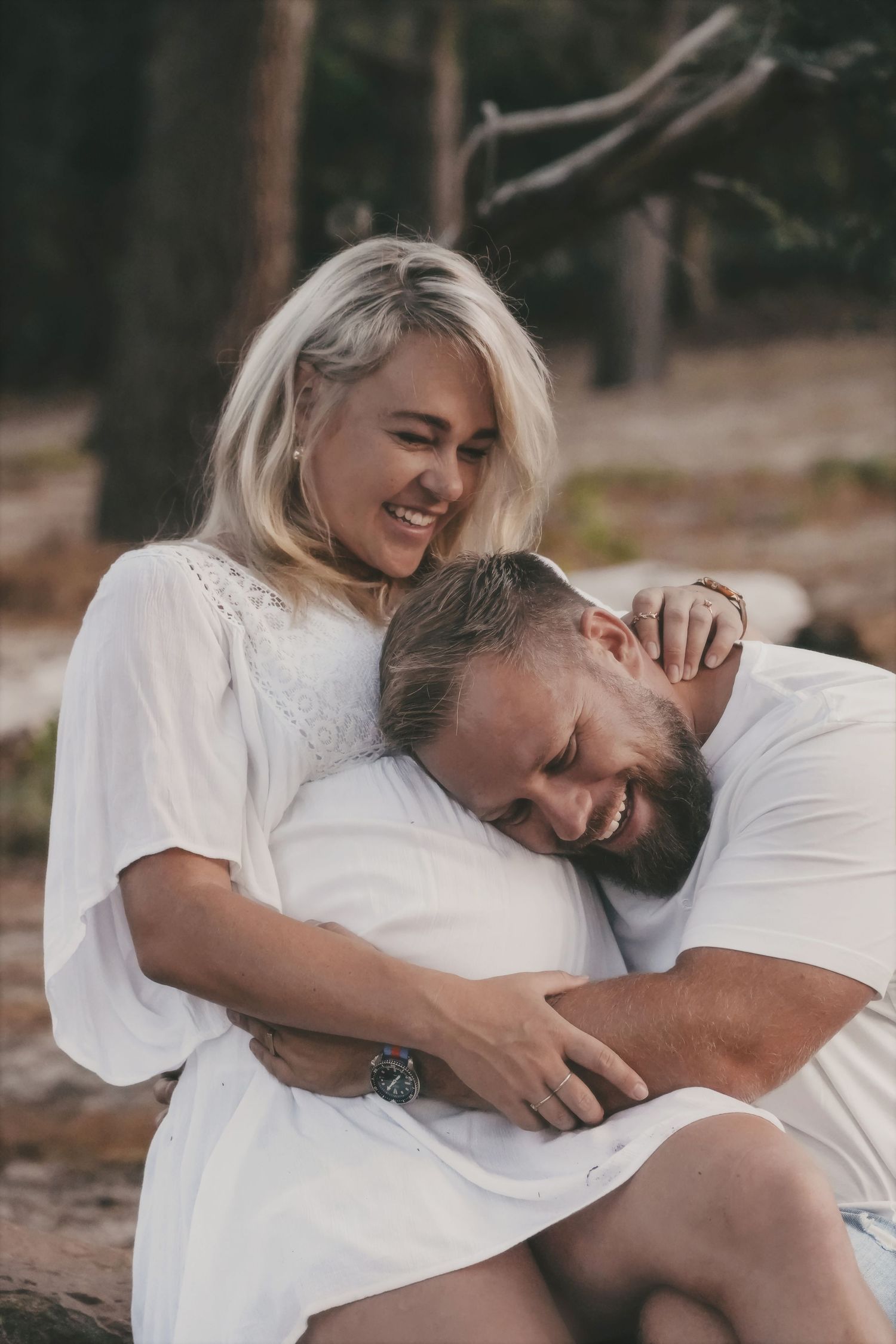 Smiling woman winking as her partner rests his head against her bump