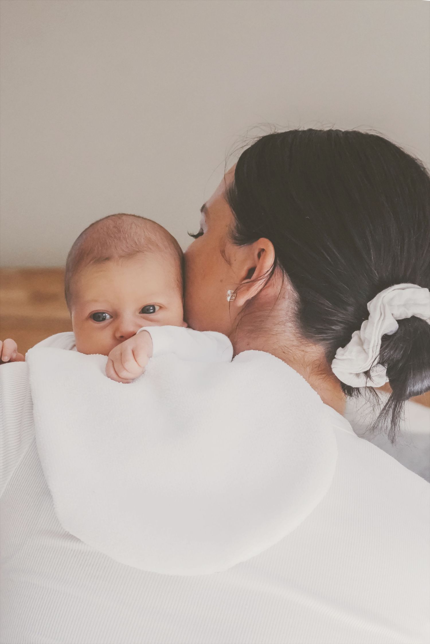 Newborn gazing at the camera over mum's shoulder as she kisses their cheek