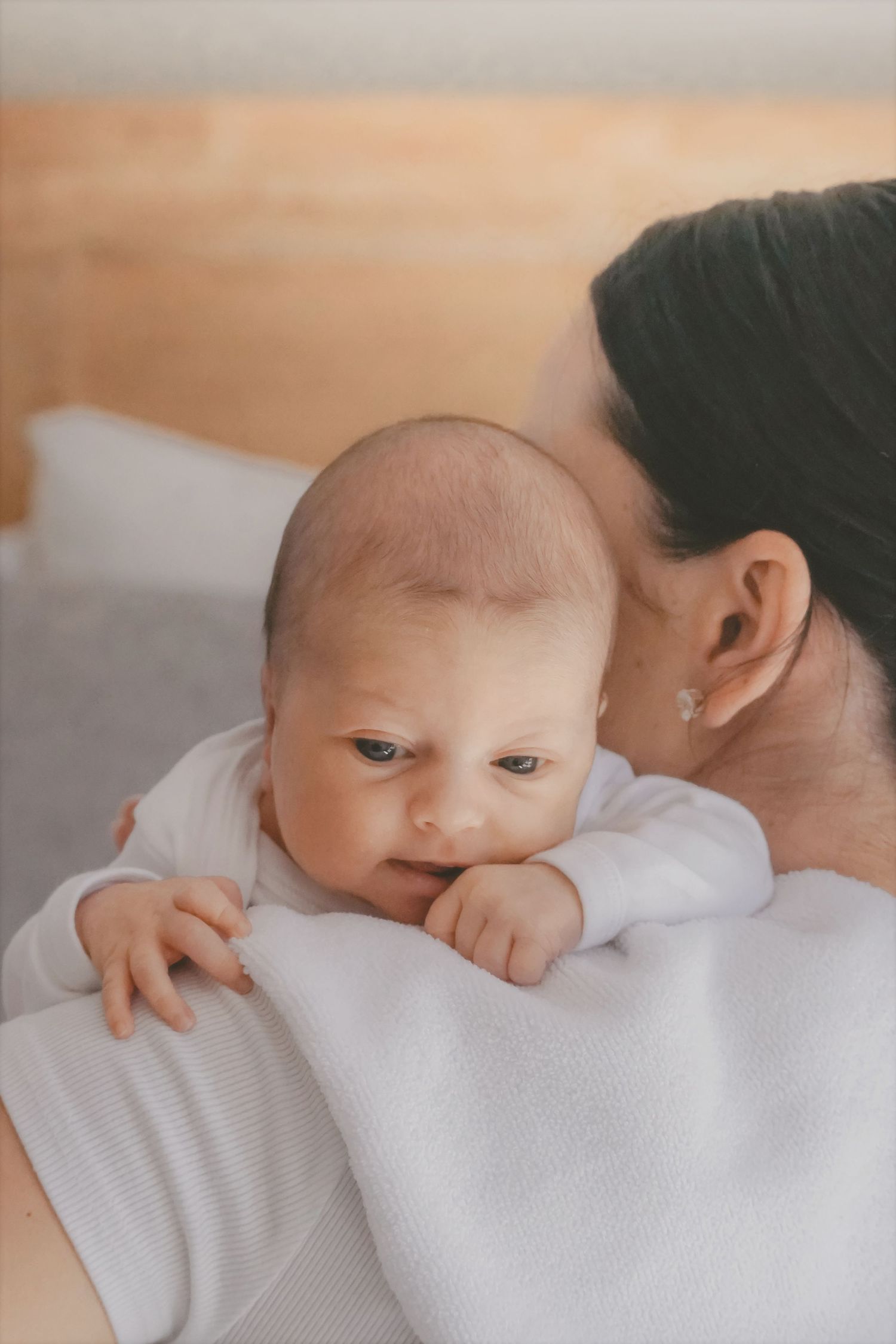 Close-up of a newborn resting on mum's shoulder with tiny hands tucked up