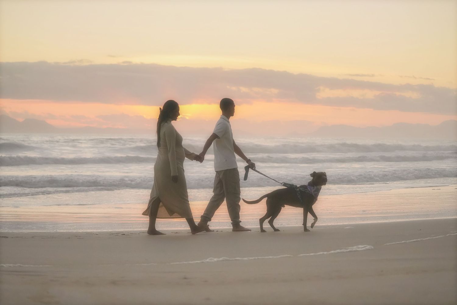 Couple walking their dog along the shoreline at sunset in Cape Town