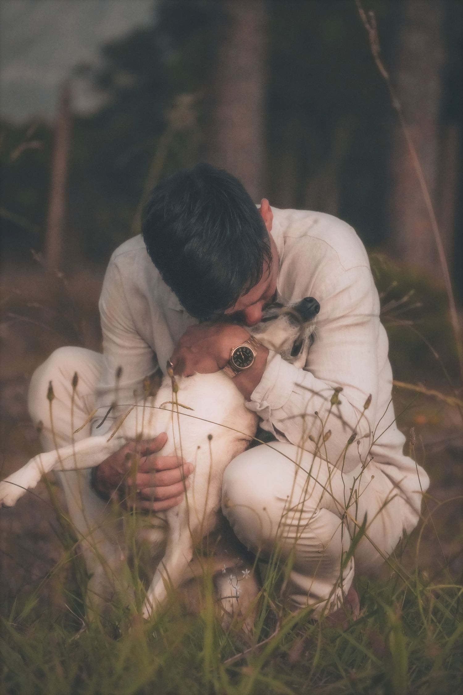 Man crouching in the grass to hug a white dog