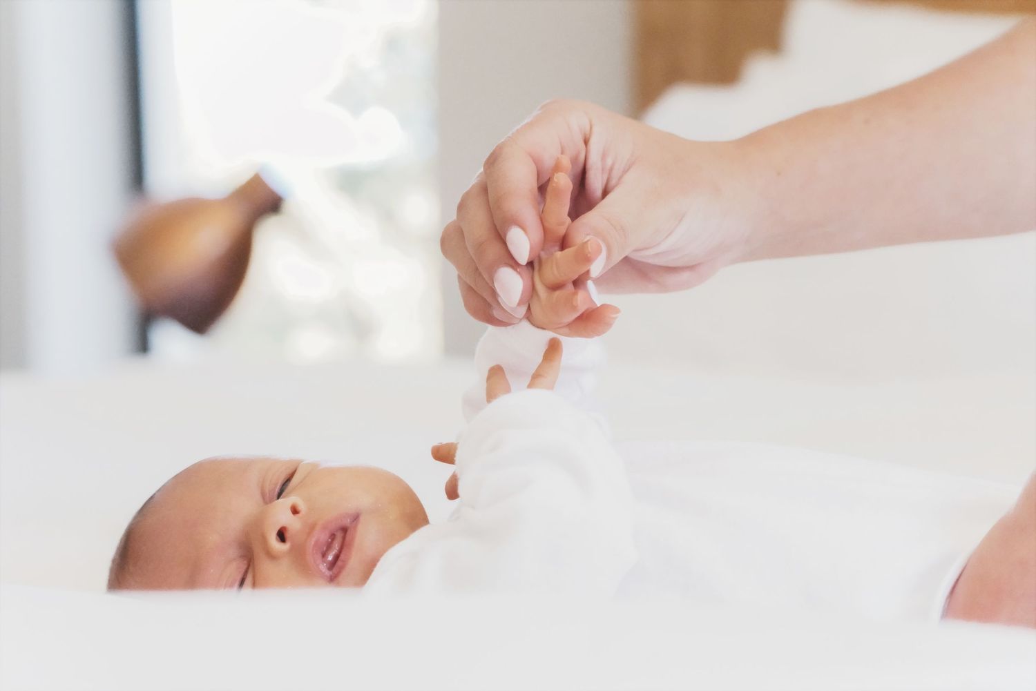 Mother's hand holding a newborn's tiny hand as they lie on a white bed