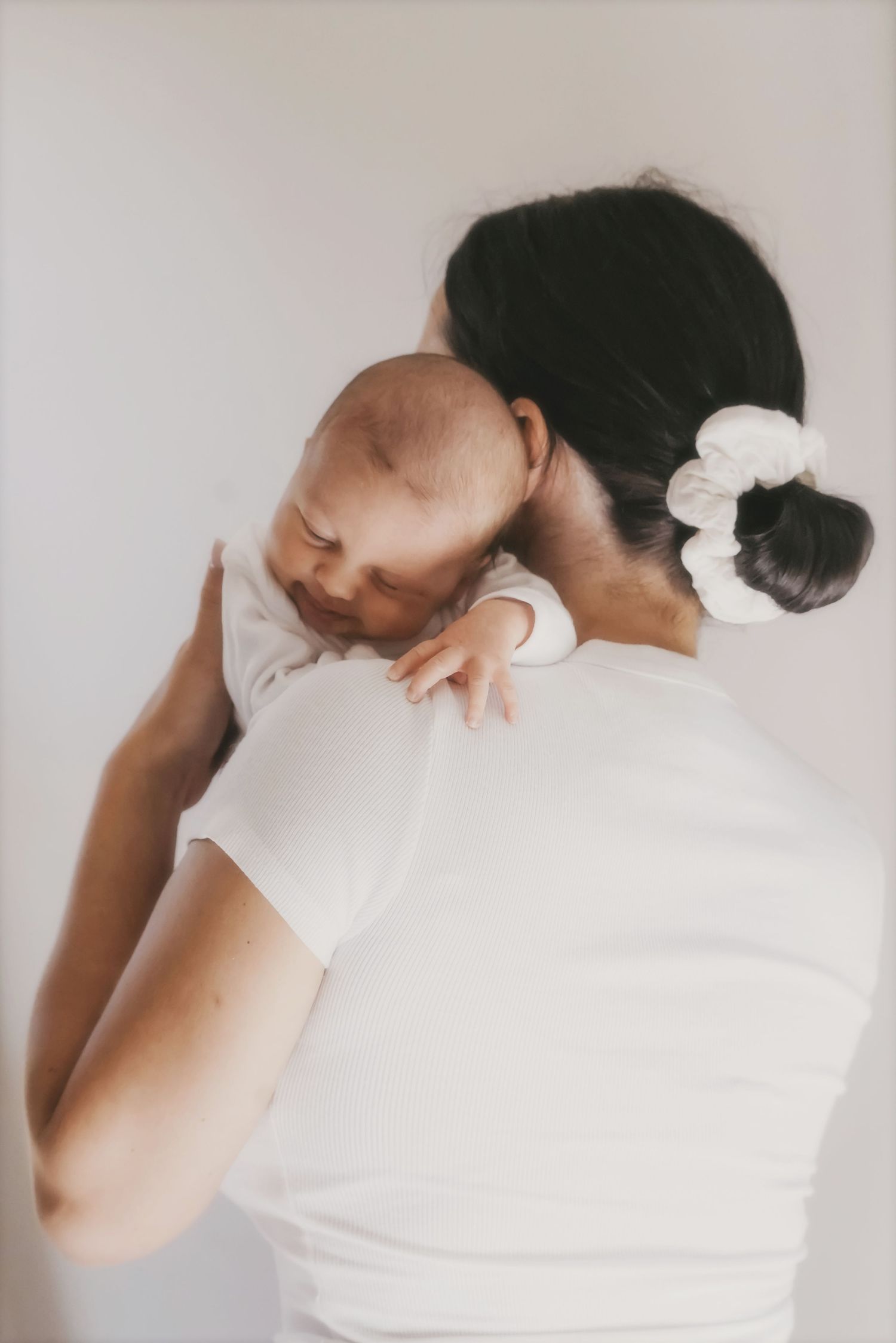 Mother holding a sleeping newborn against her shoulder, seen from behind