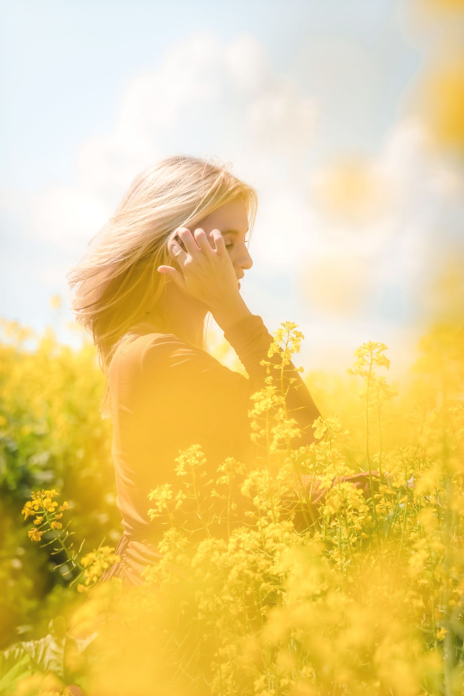 Woman with hair blowing, one hand to her head, in canola under a cloudy sky