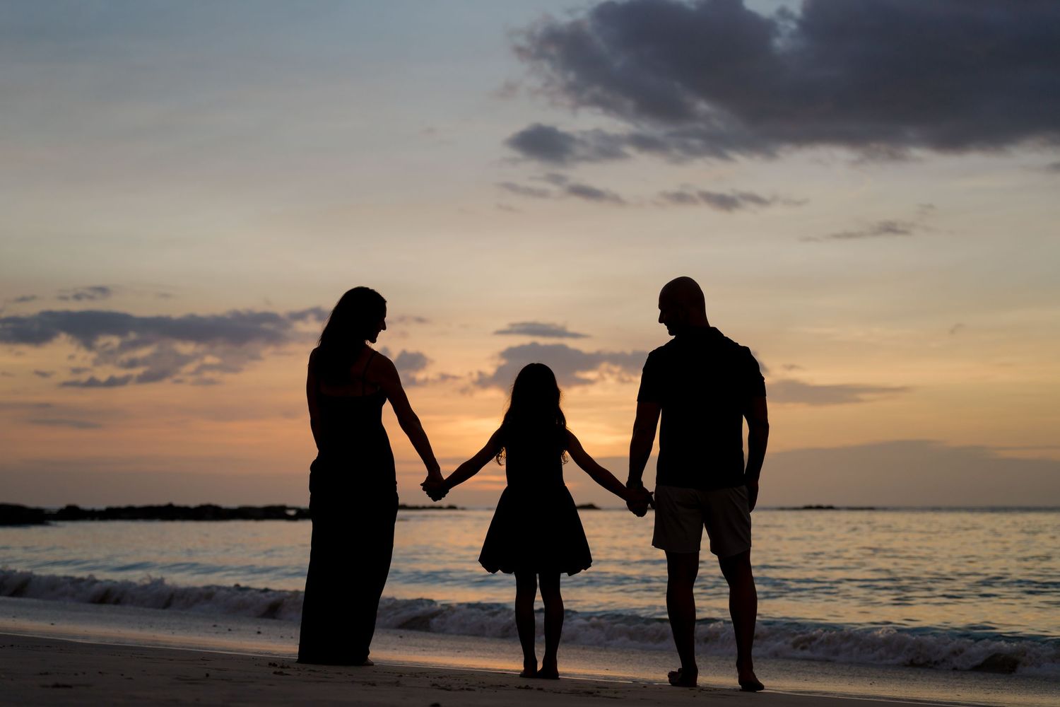 Family of three holding hands in silhouette during sunset at Four Seasons Resort Peninsula Papagayo, Costa Rica.