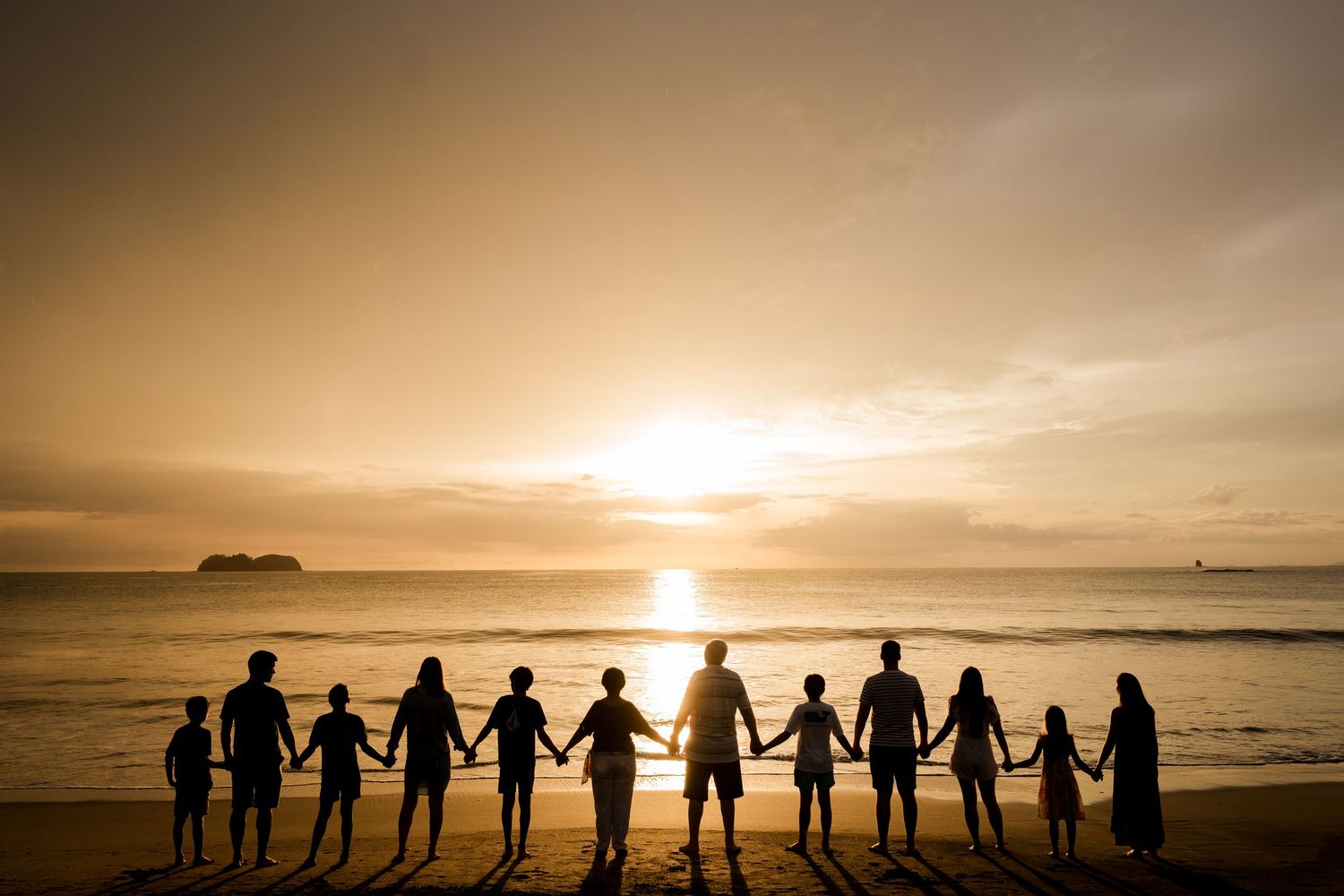 Large multi-generational family holding hands along the beach at sunset during a vacation photography session in Costa Rica.