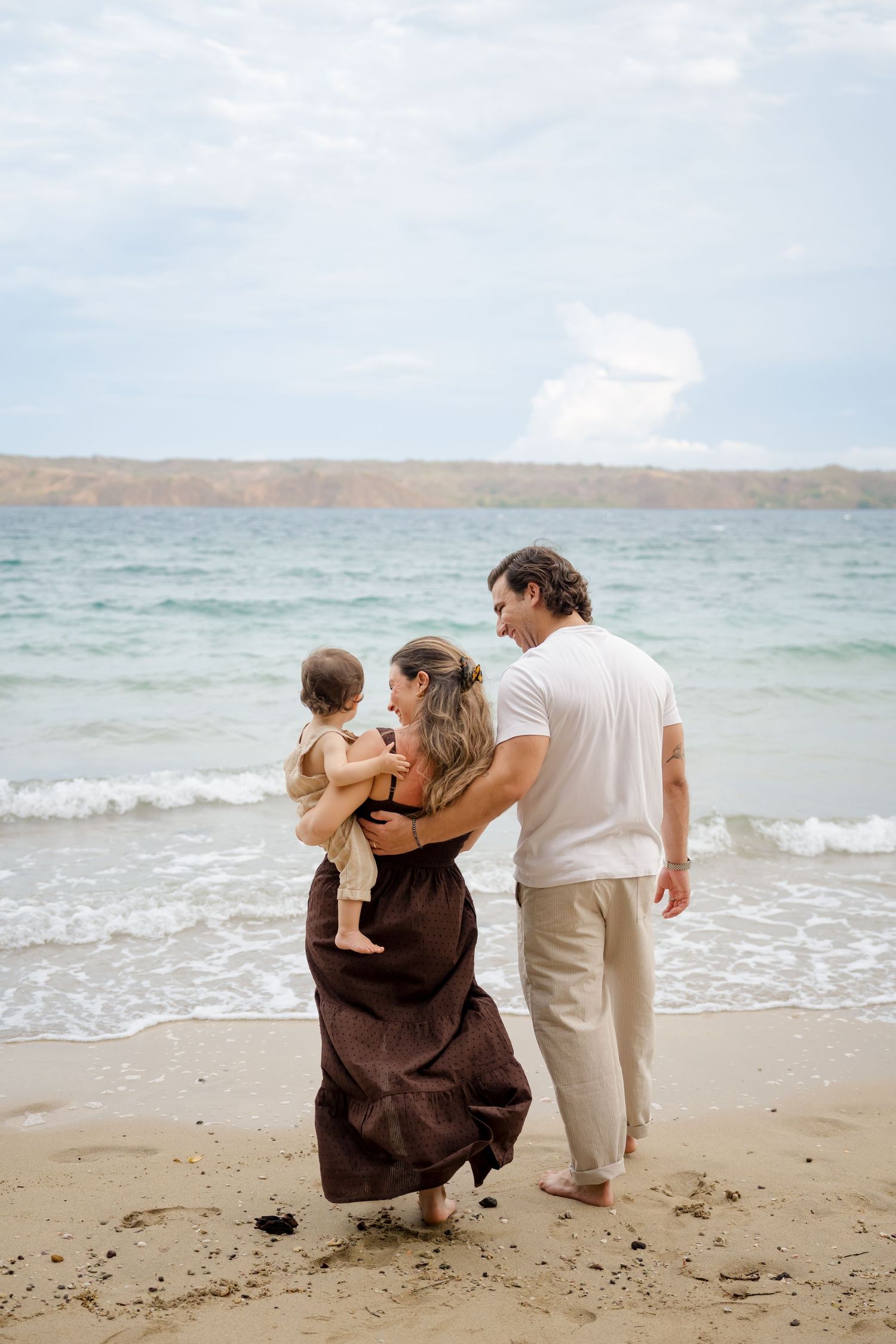 Parents walking with their young child along the beach during a family photography session at Andaz Peninsula Papagayo, Costa Rica.