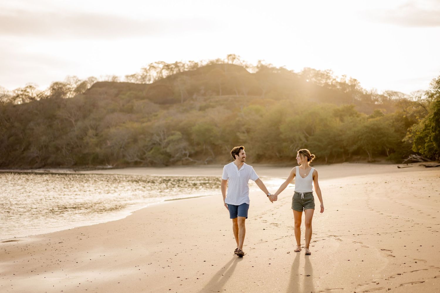 Couple holding hands and walking along Playa Hermosa during a golden hour photography session in Guanacaste, Costa Rica.