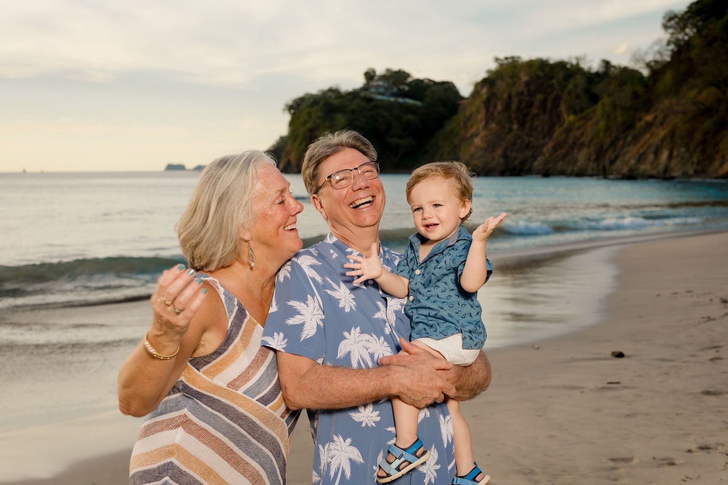 Grandparents laughing with their grandchild during a relaxed family vacation photography session on the beach in Costa Rica.