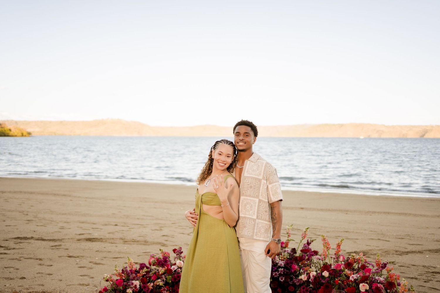 Newly engaged couple posing by their floral proposal setup on the beach at Andaz Costa Rica.