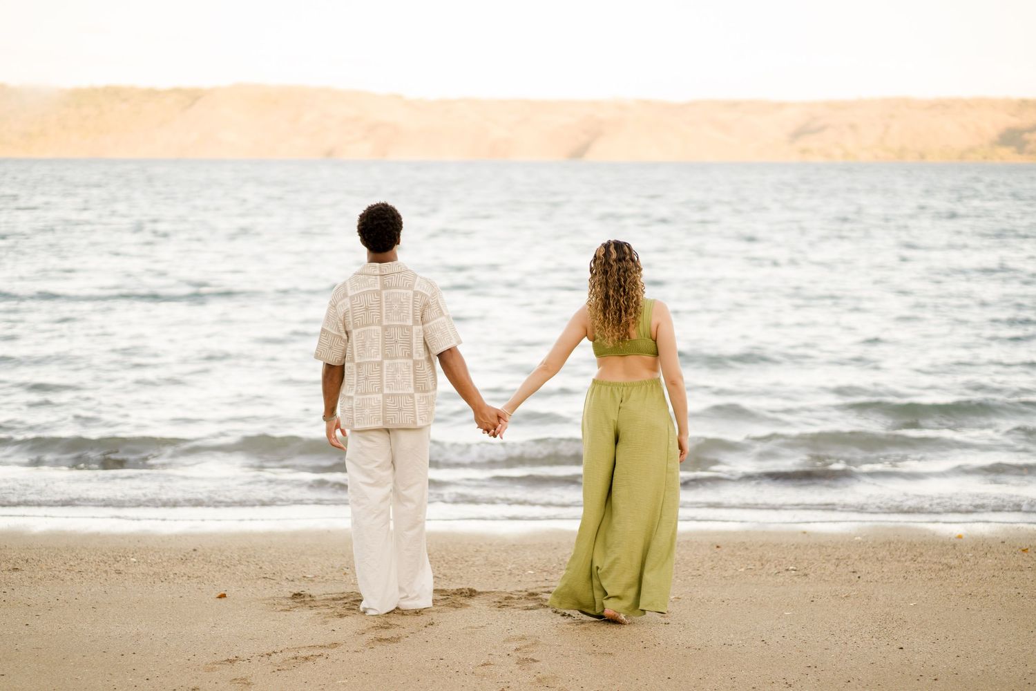 Newly engaged couple holding hands and looking toward the ocean during a beach session at Andaz Costa Rica.