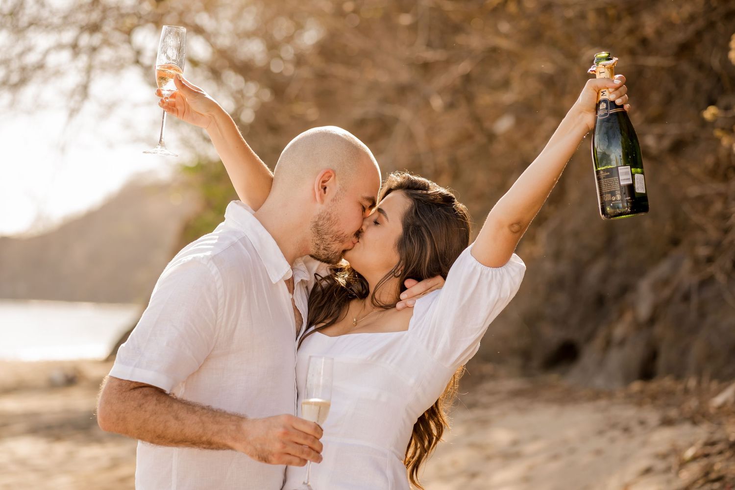 Couple kissing and celebrating with champagne during a romantic beach photography session at El Mangroove, Costa Rica.