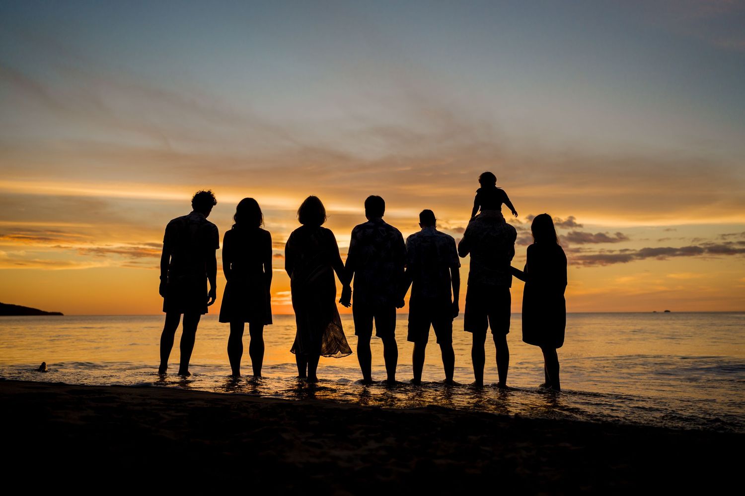 Multi-generational family silhouetted against a colorful sunset during a beach photography session in Costa Rica.