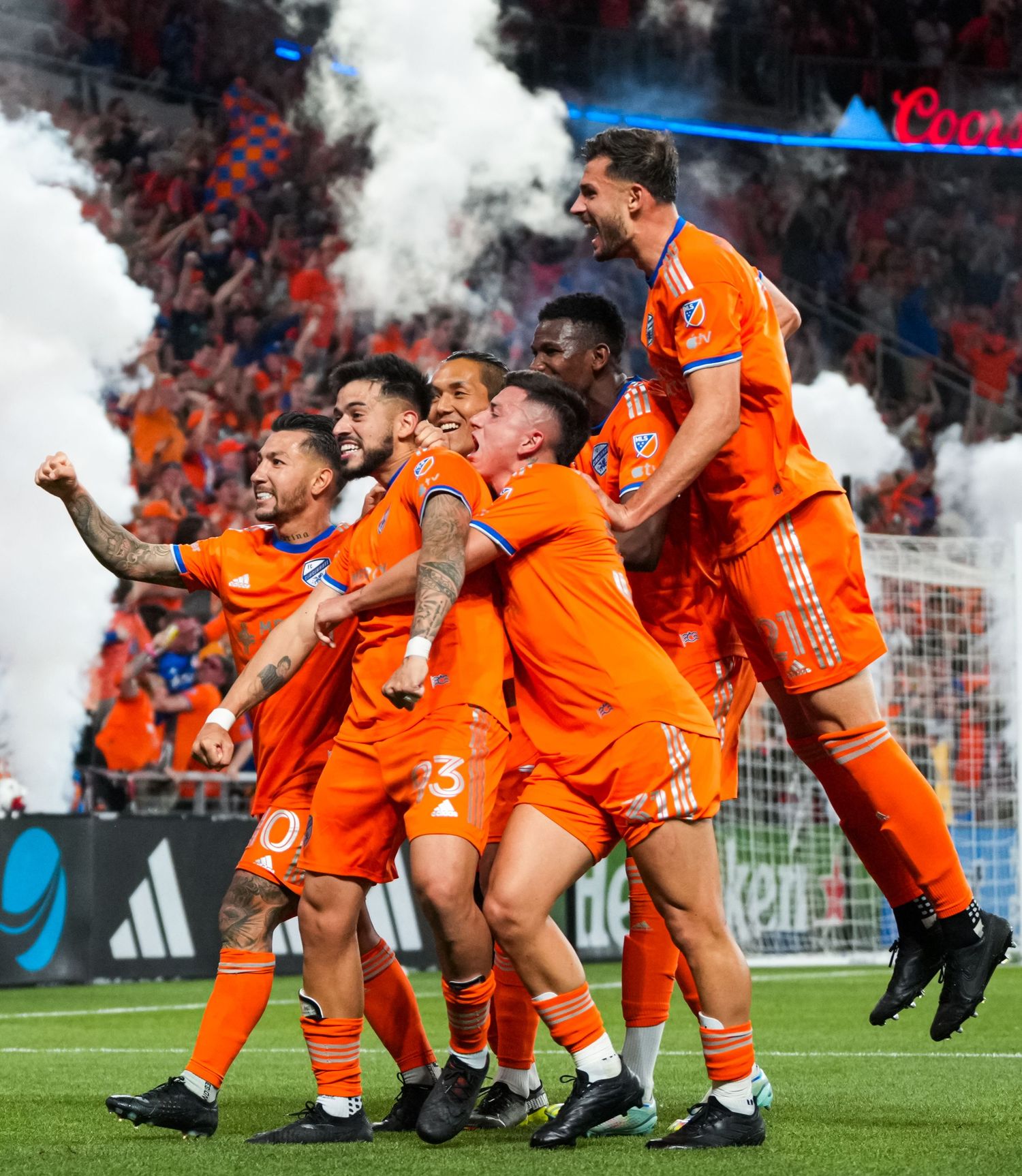 FC Cincinnati players in orange uniforms celebrating together in front of a crowd.