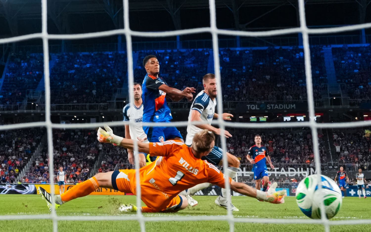 Goal-line view of players contesting a scoring chance in front of a crowded stadium.