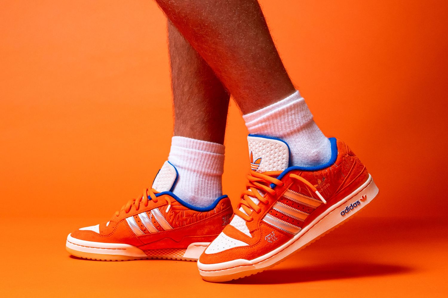 Person wearing orange Adidas sneakers with white socks, photographed against an orange background.