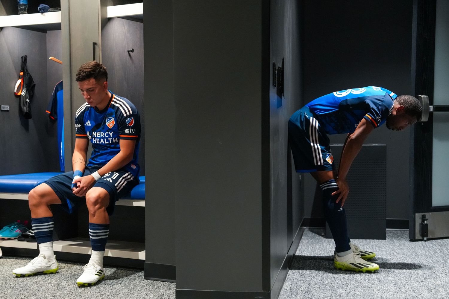 Two FC Cincinnati players preparing in a locker room before a match.