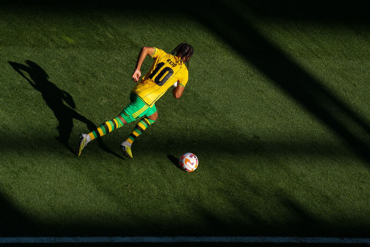 Soccer player in a yellow uniform dribbling a ball across the field from an overhead perspective.