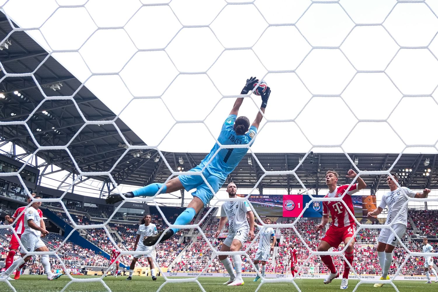 Goalkeeper leaps toward the ball while players watch from inside the penalty area during a soccer match.