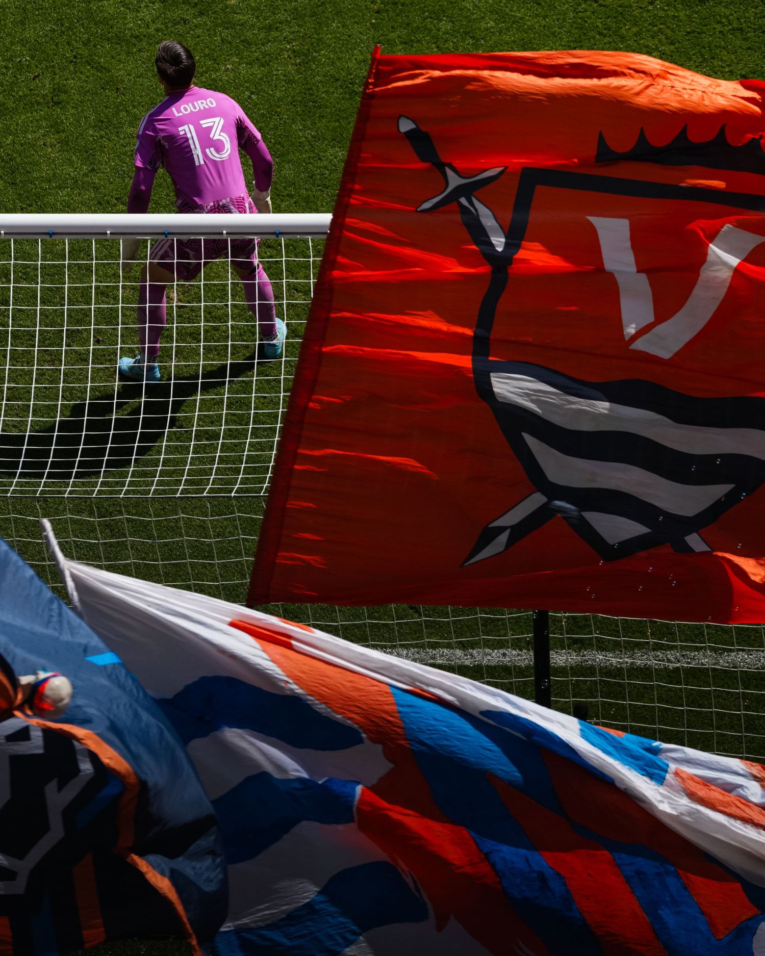 Large supporter flags wave behind a goal as a goalkeeper waits on the field before a match.