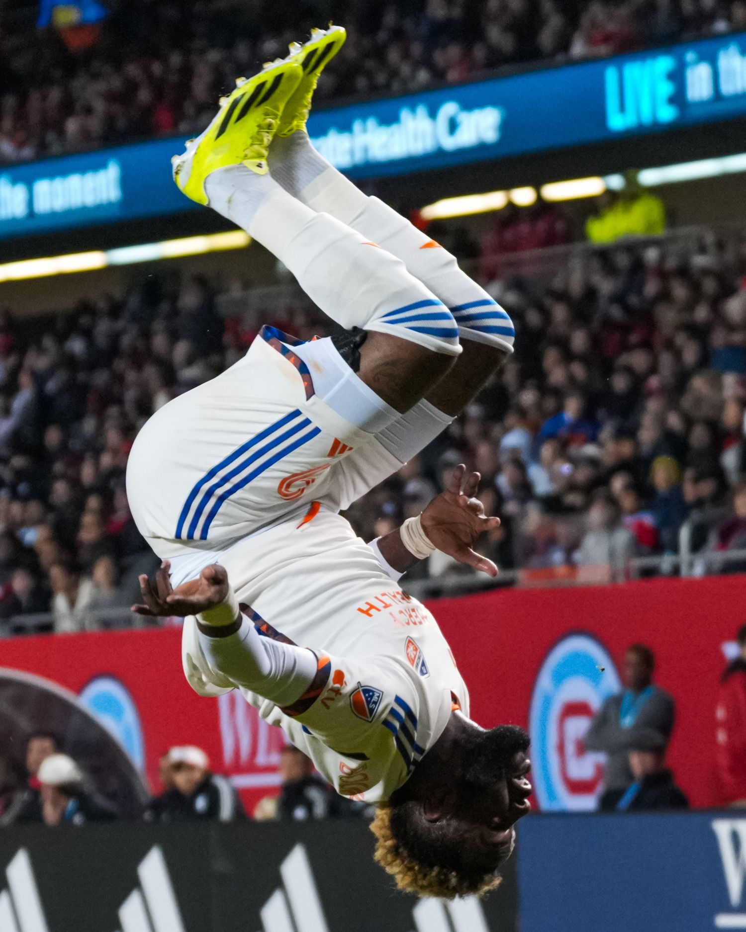 Soccer player in a white uniform performs a midair flip during a match celebration.