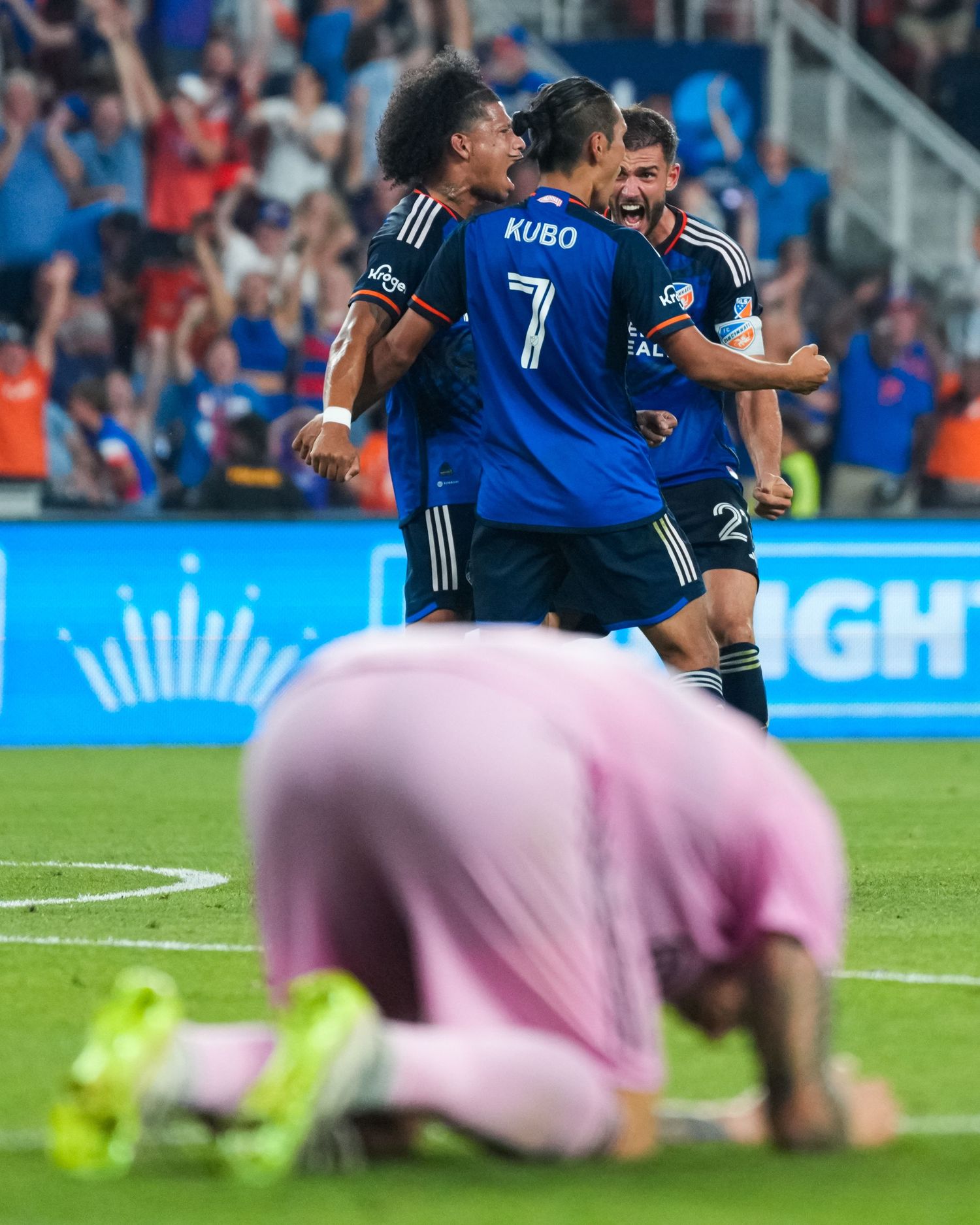 FC Cincinnati players celebrating while an opposing player kneels in the foreground.